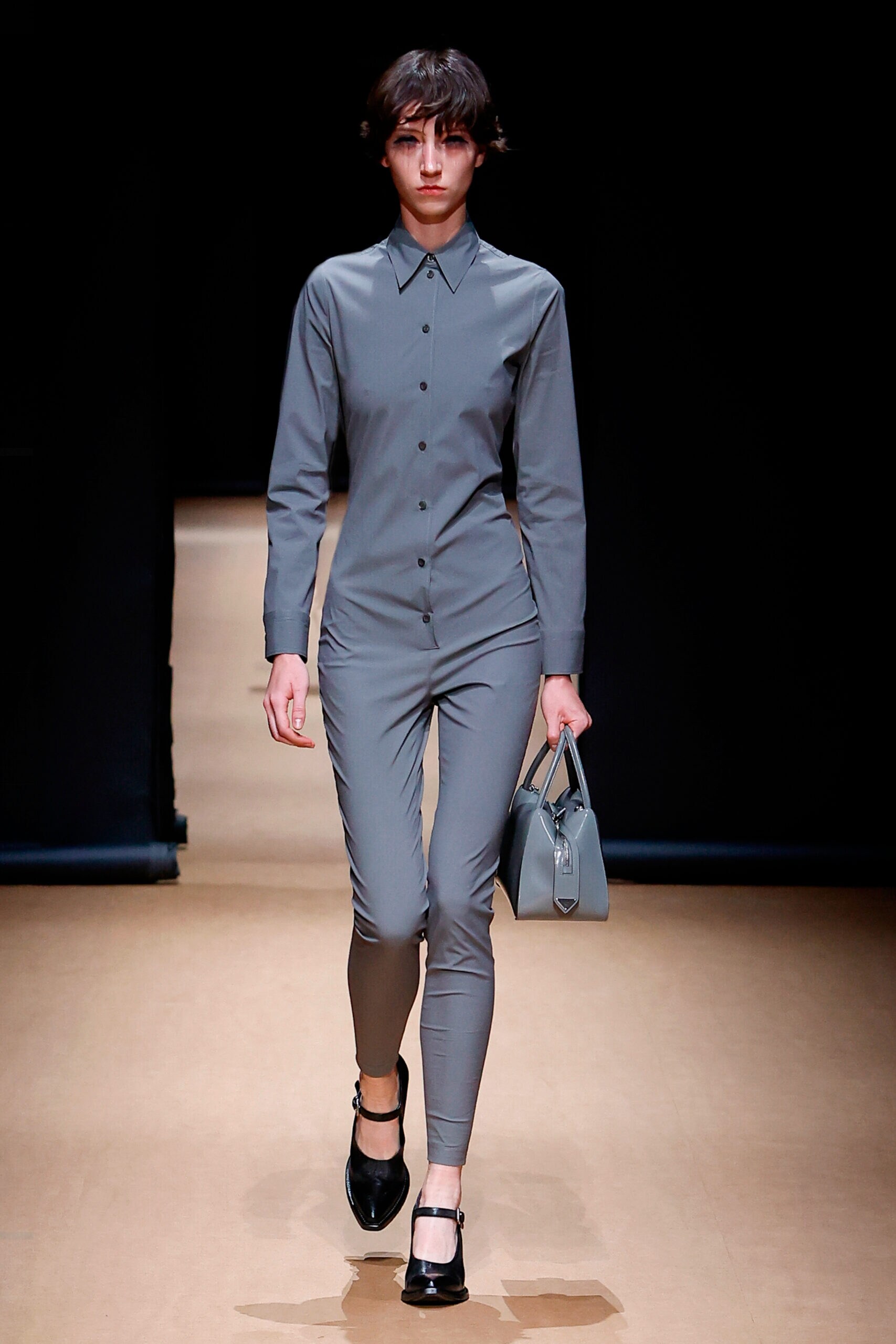 Ein weibliches Model läuft in einem grauen Jumpsuit über einen Laufsteg Ein weibliches Model läuft in einem grauen Jumpsuit über einen Laufsteg