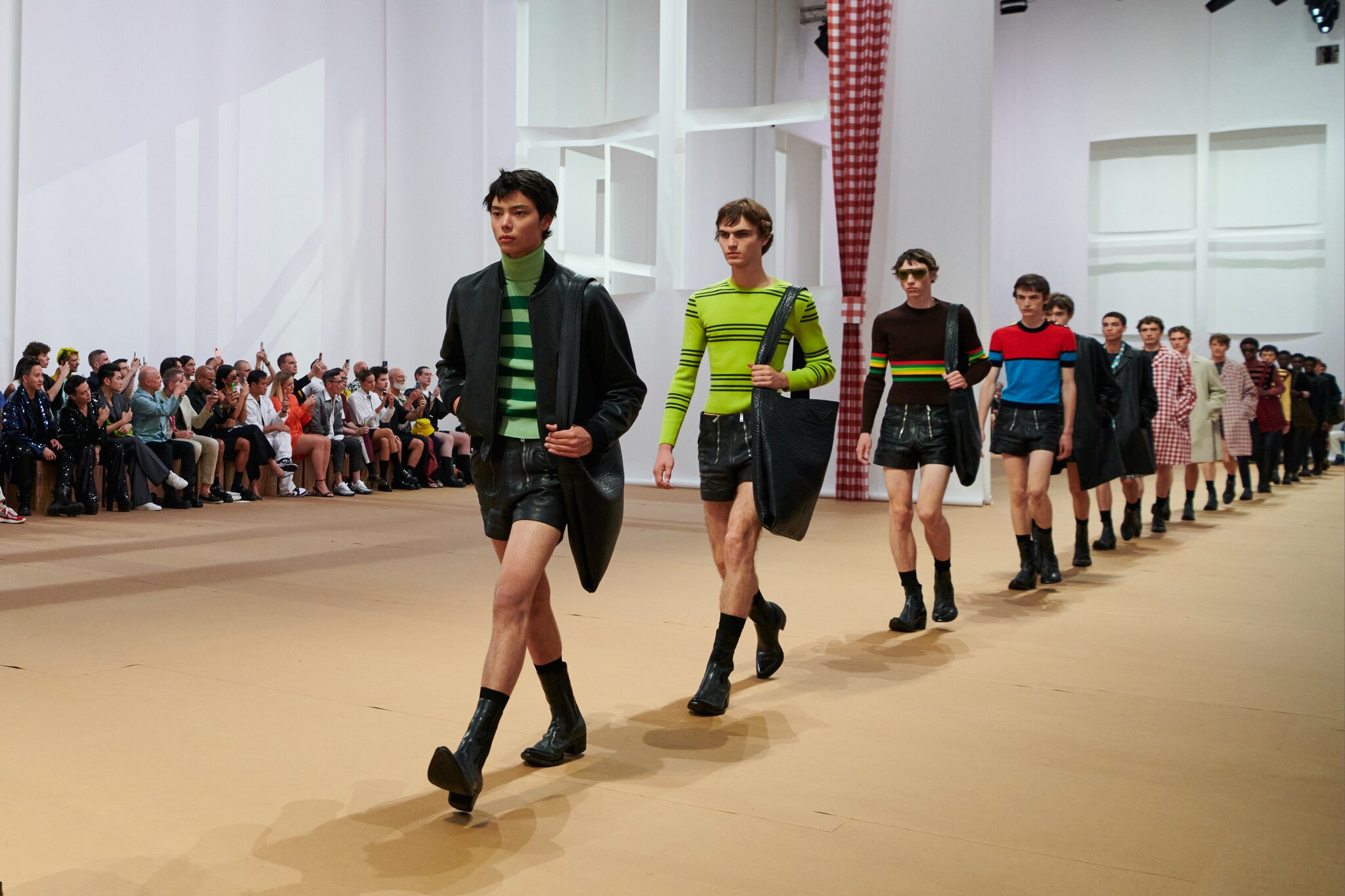 Männliche Models in Ledershorts laufen in Reihe auf einem Catwalk Männliche Models in Ledershorts laufen in Reihe auf einem Catwalk