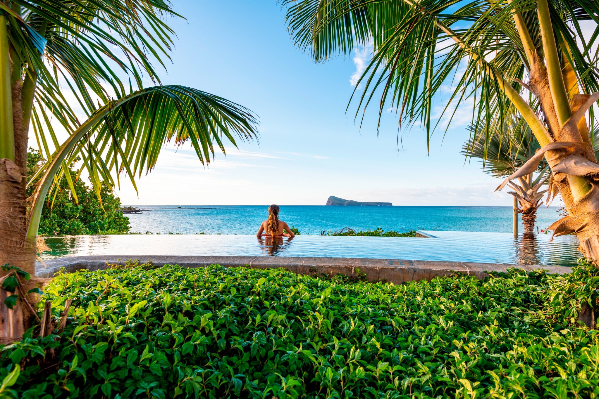 Rückansicht einer Frau in einem Pool am Meer, umgeben von tropischer Vegetation