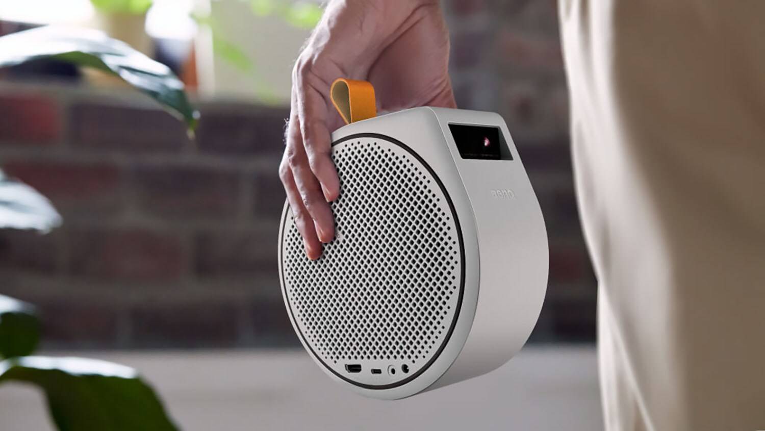 Close-up of a small, round projector with a built-in speaker, carried in a person's hand.