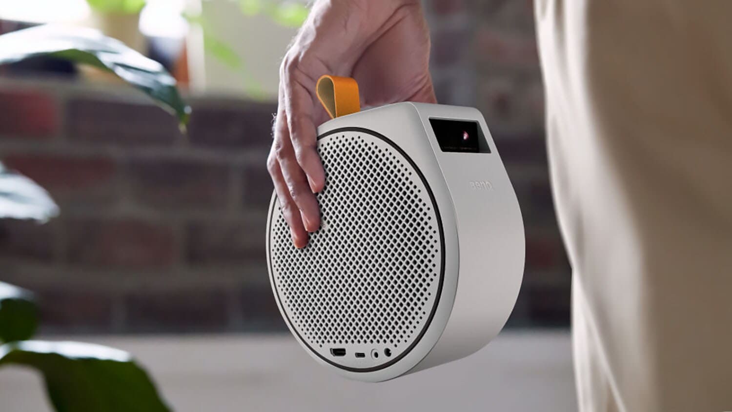 Close-up of a small, round projector with a built-in speaker, carried in a person's hand. Close-up of a small, round projector with a built-in speaker, carried in a person's hand.