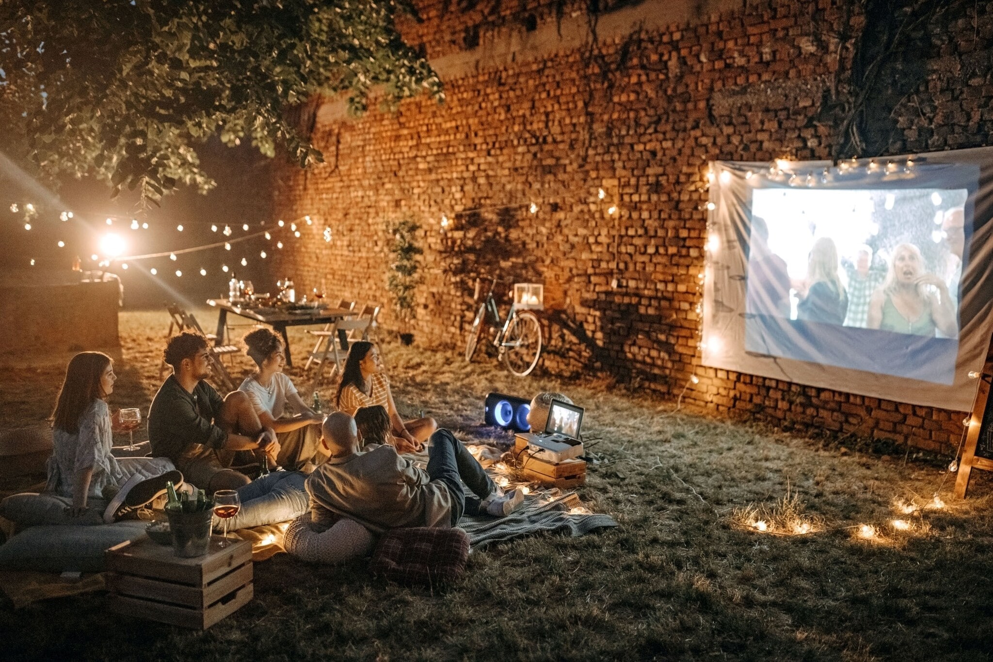 Eine Personengruppe sieht mit einem Mini-Beamer einen Film an einer Mauer im Garten. Eine Personengruppe sieht mit einem Mini-Beamer einen Film an einer Mauer im Garten.