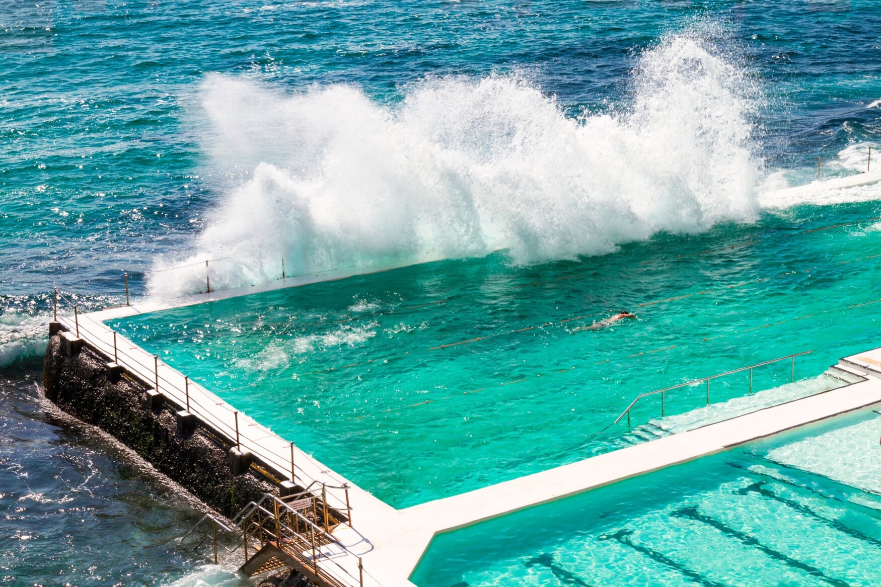 Männliche Athleten schwimmen in einem Meerwasserpool, an dem sich von außen die Wellen brechen. Männliche Athleten schwimmen in einem Meerwasserpool, an dem sich von außen die Wellen brechen.