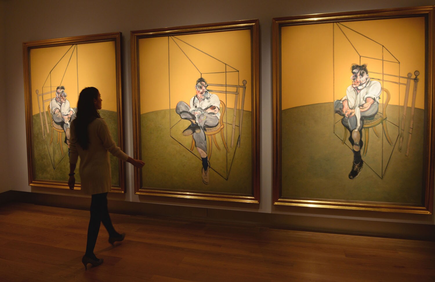 Eine Frau betrachtet drei Bilder von Francis Bacon in einem Museum