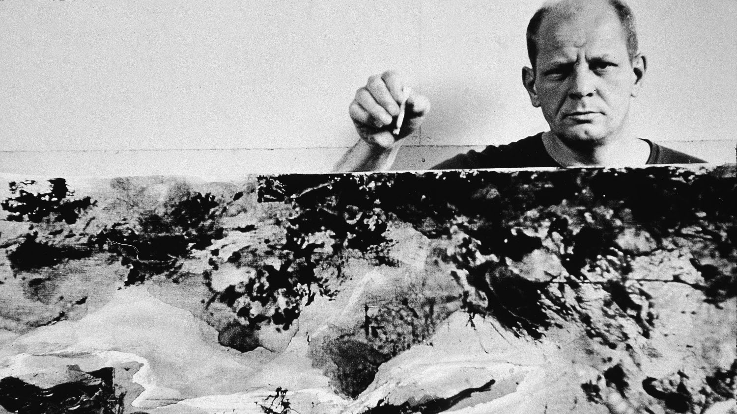 Schwarzweißaufnahme des Künstlers Jackson Pollock mit einem seiner abstrakten Bilder Schwarzweißaufnahme des Künstlers Jackson Pollock mit einem seiner abstrakten Bilder