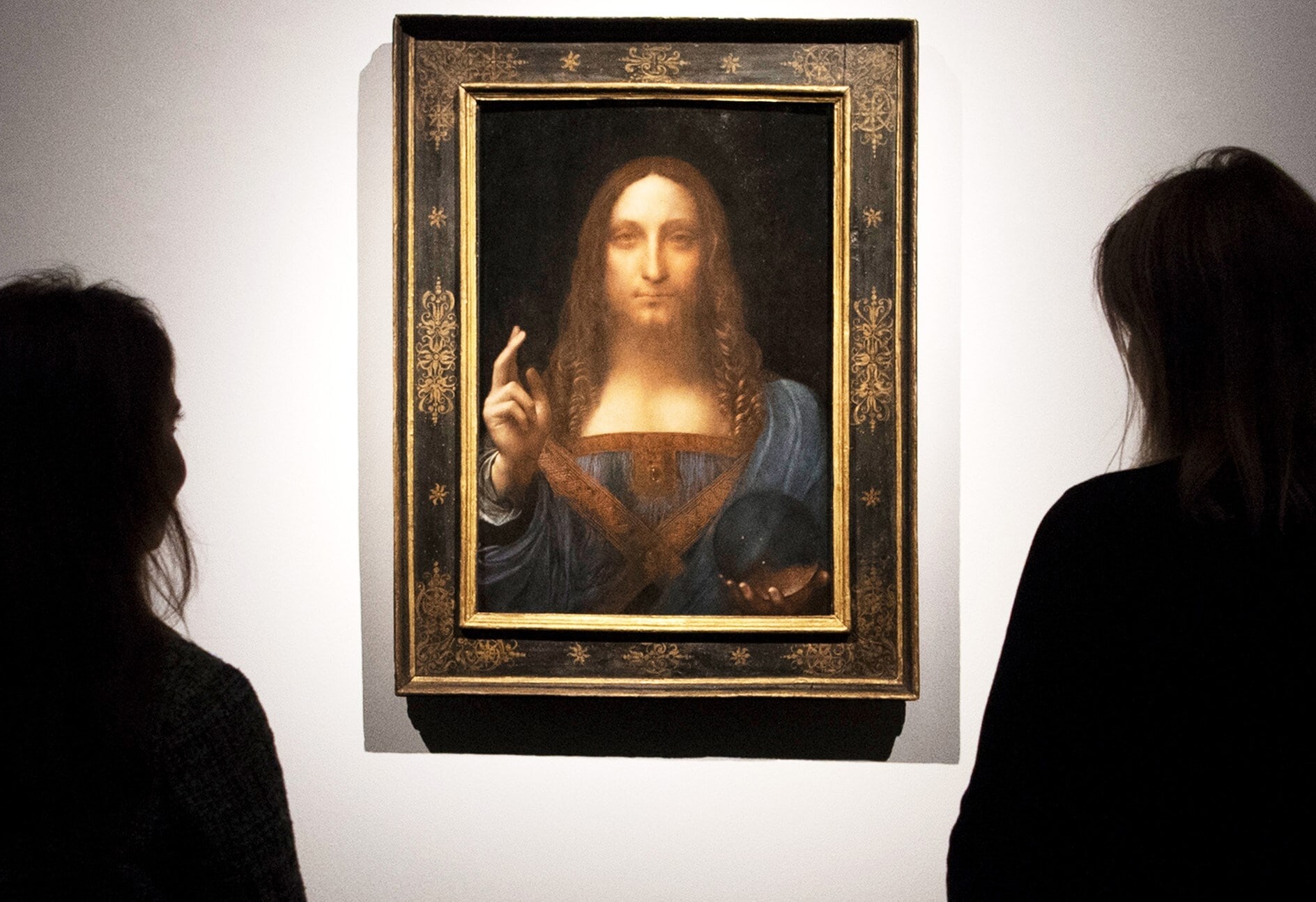 Das Gemälde Salvator Mundi an einer Wand, davor zwei Betrachterinnen im Anschnitt Das Gemälde Salvator Mundi an einer Wand, davor zwei Betrachterinnen im Anschnitt
