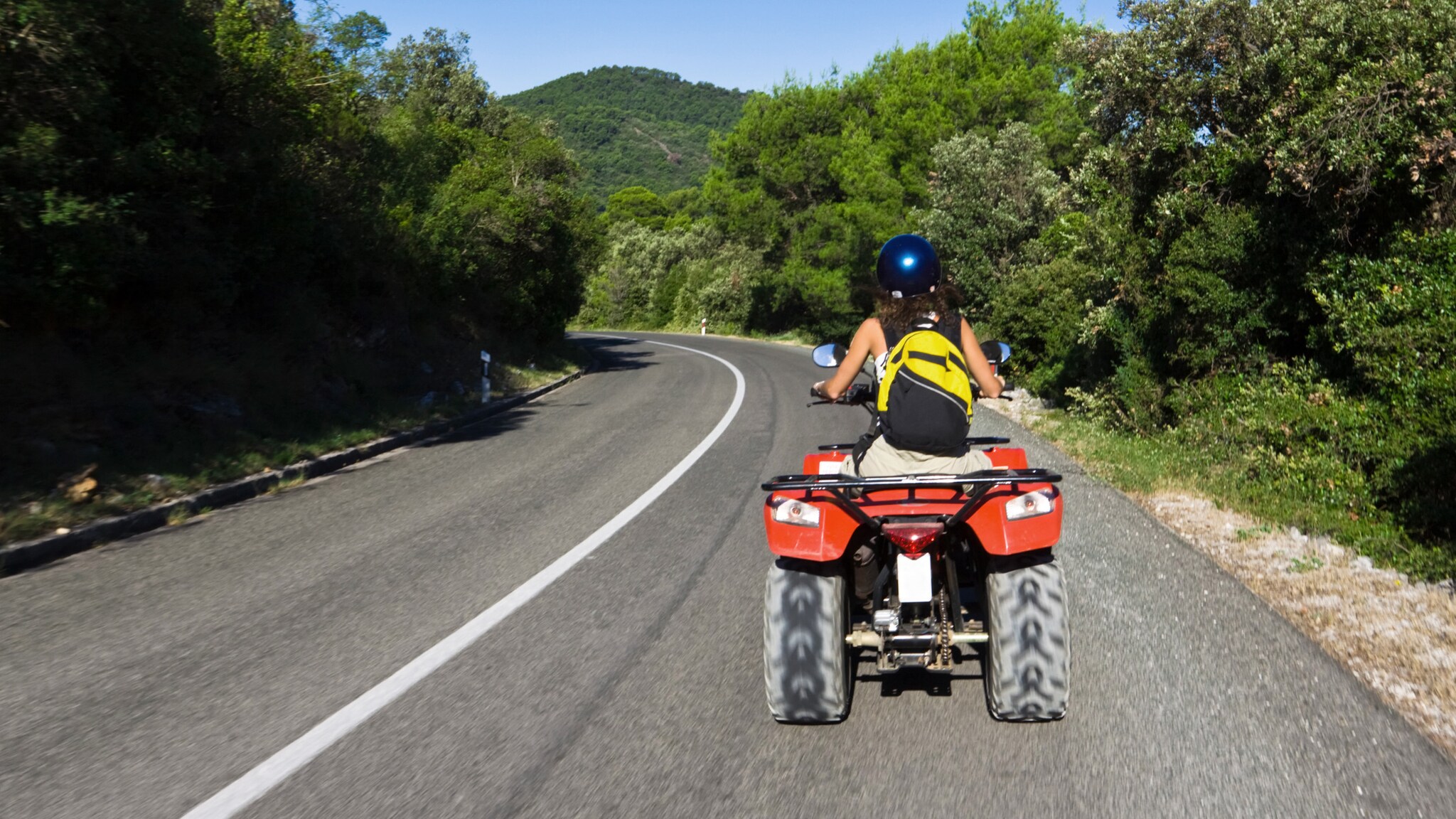 Eine Frau in sommerlicher Kleidung fährt auf einem Quad eine Straße entlang Eine Frau in sommerlicher Kleidung fährt auf einem Quad eine Straße entlang