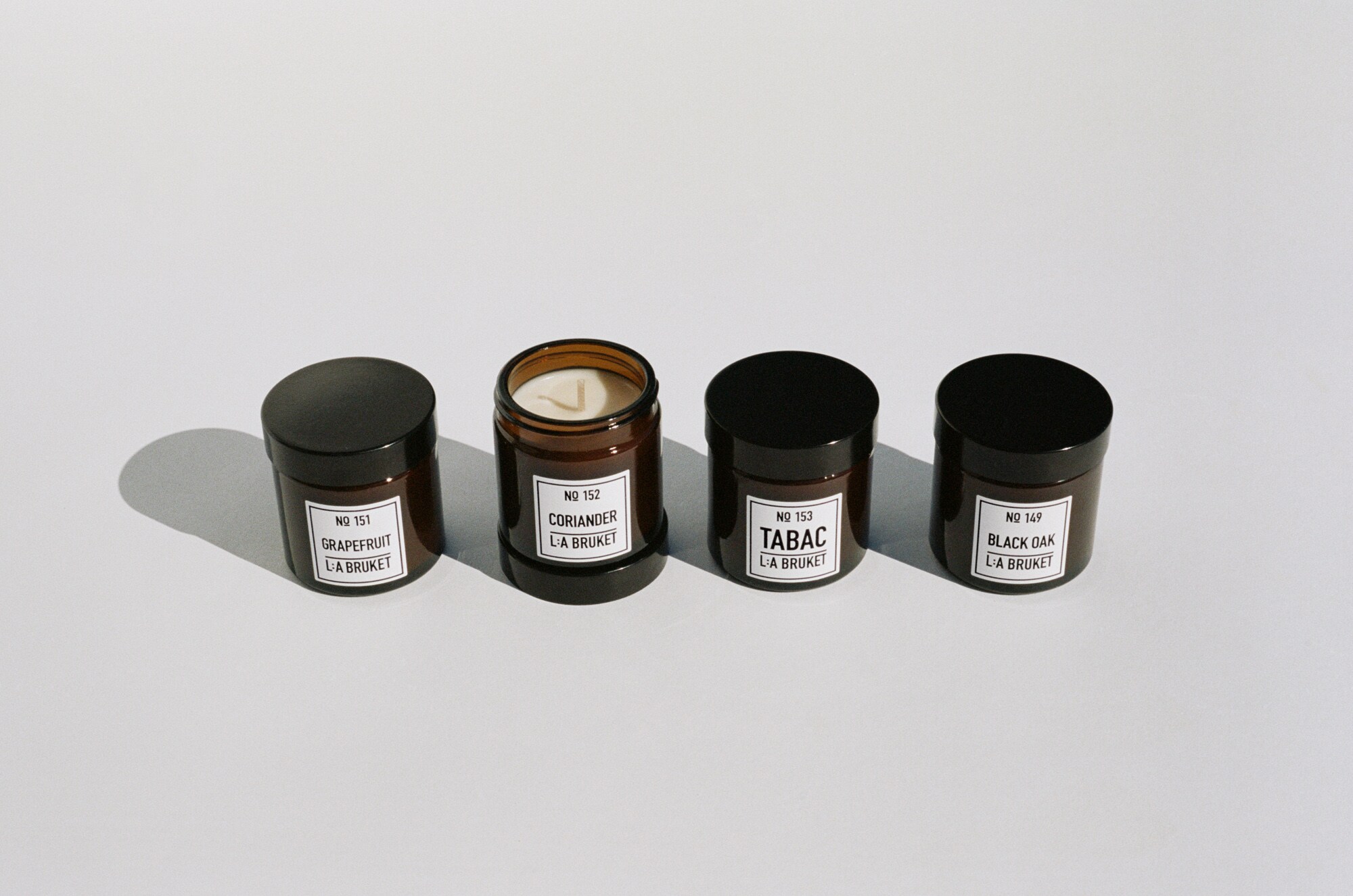 Vier Kerzen aus hellem Wachs in dunkelbraunen Gläsern mit schwarzen Verschlusskappen und weißen Etiketten. Vier Kerzen aus hellem Wachs in dunkelbraunen Gläsern mit schwarzen Verschlusskappen und weißen Etiketten.