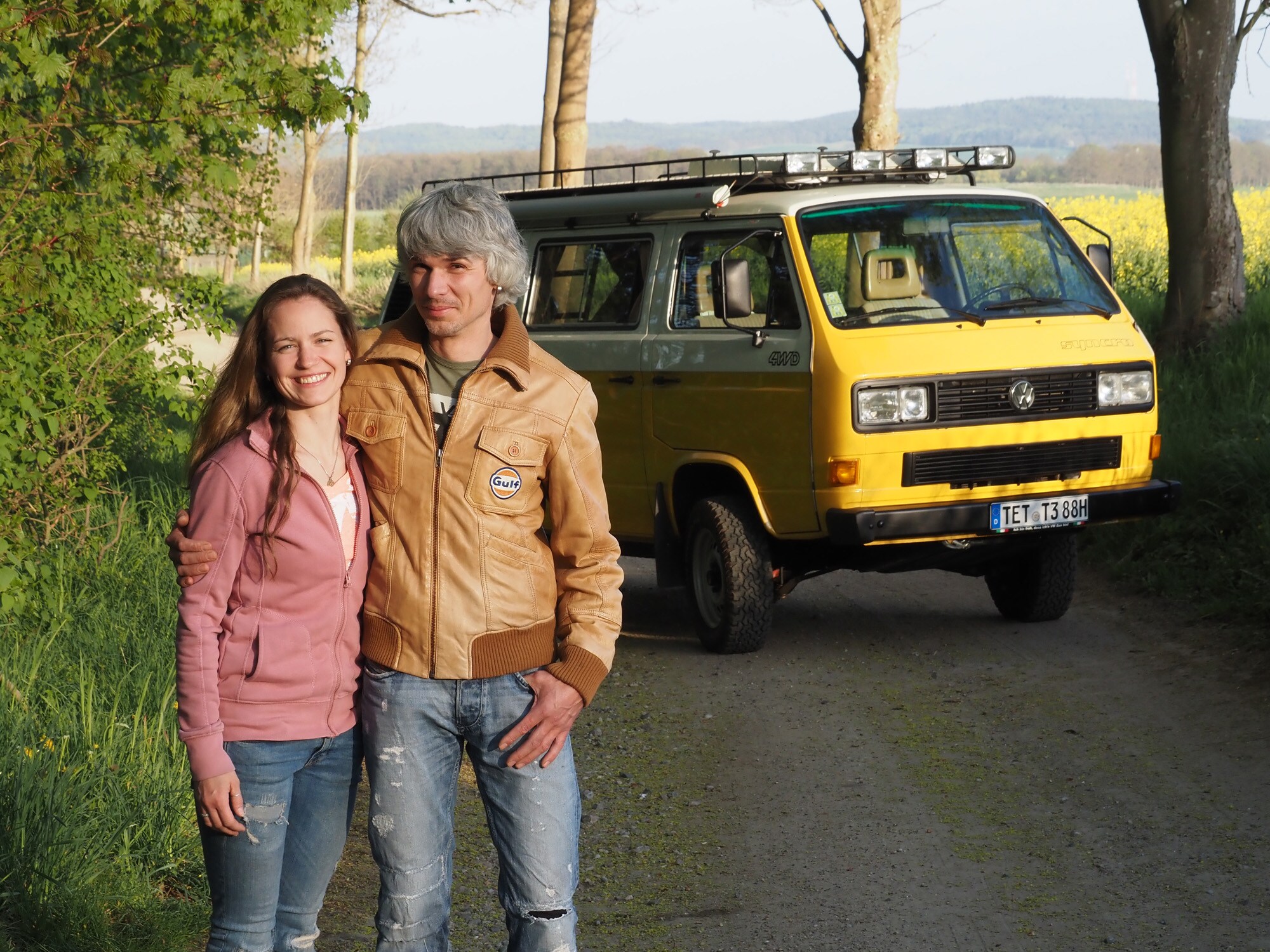 Ein Mann und eine Frau stehen vor einem gelben Bulli in der Natur Ein Mann und eine Frau stehen vor einem gelben Bulli in der Natur
