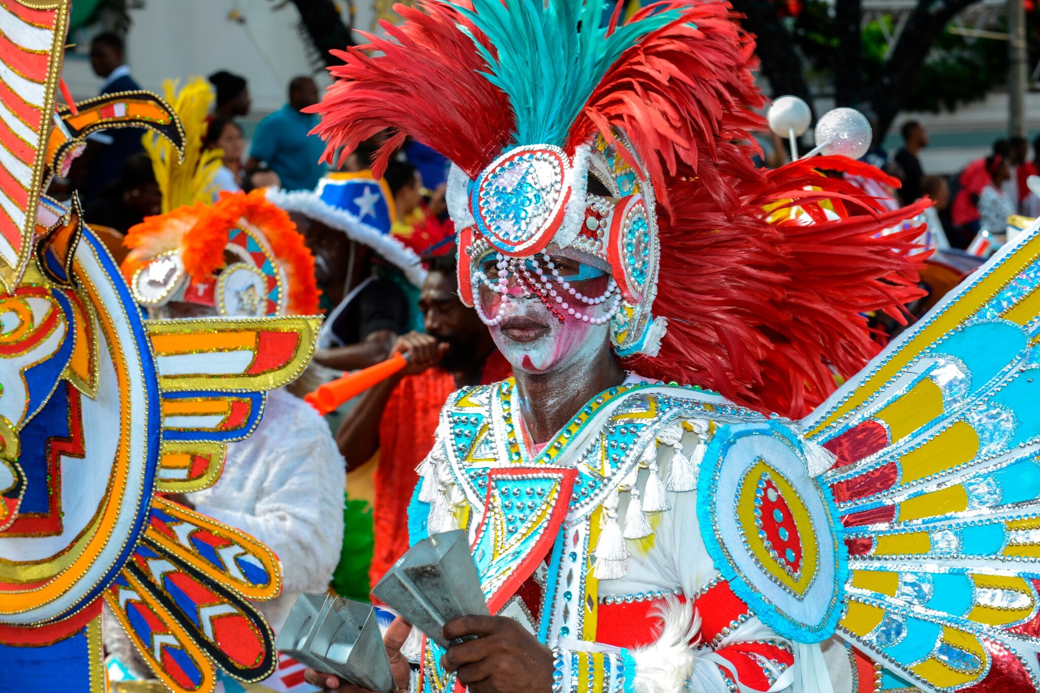 Kostümierte Person mit rotem Federschmuck auf dem Kopf und weiß geschminktem Gesicht im bunten Gewand Kostümierte Person mit rotem Federschmuck auf dem Kopf und weiß geschminktem Gesicht im bunten Gewand