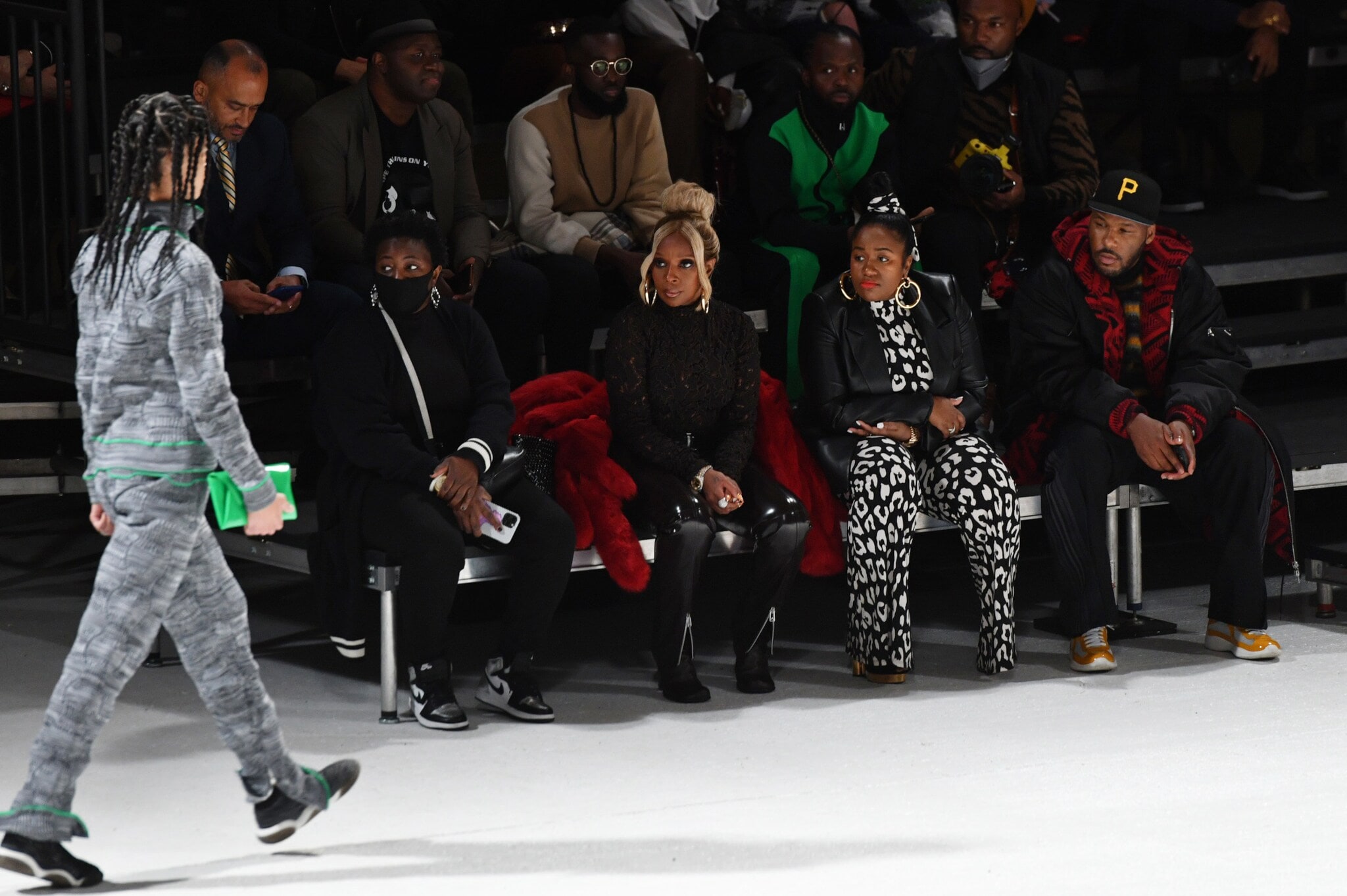 Mehrere Personen sitzen am Rand eines Laufstegs und schauen dabei zu, wie ein Model an ihnen vorbeiläuft. Mehrere Personen sitzen am Rand eines Laufstegs und schauen dabei zu, wie ein Model an ihnen vorbeiläuft.