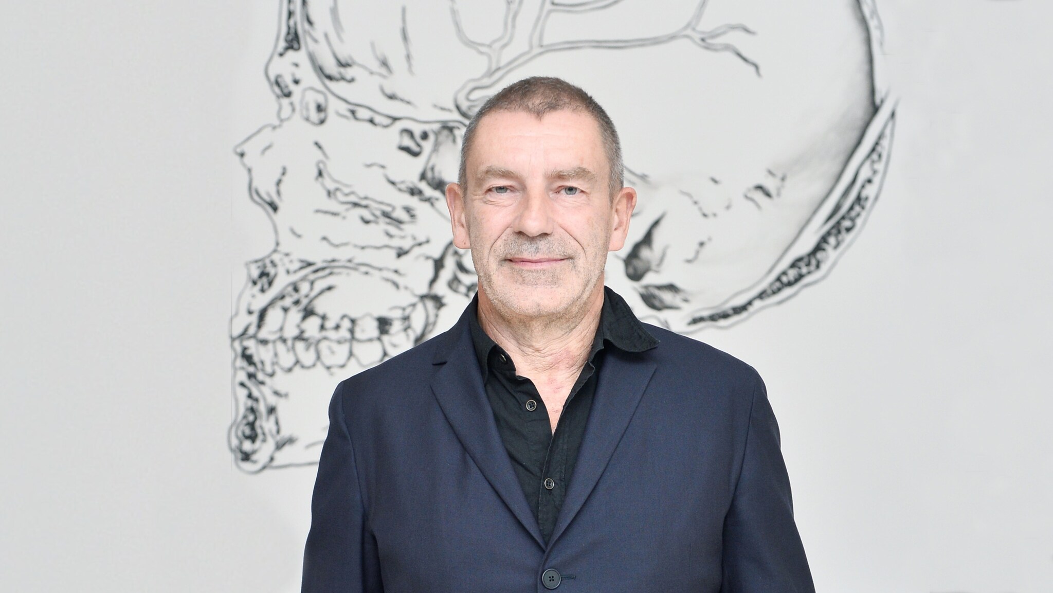 Ein Mann im Anzug steht vor einem Gemälde, das einen Schädel zeigt.