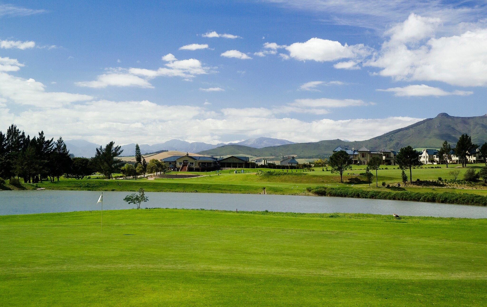 Blick auf einen Golfplatz mit See und Bergen im Hintergrund