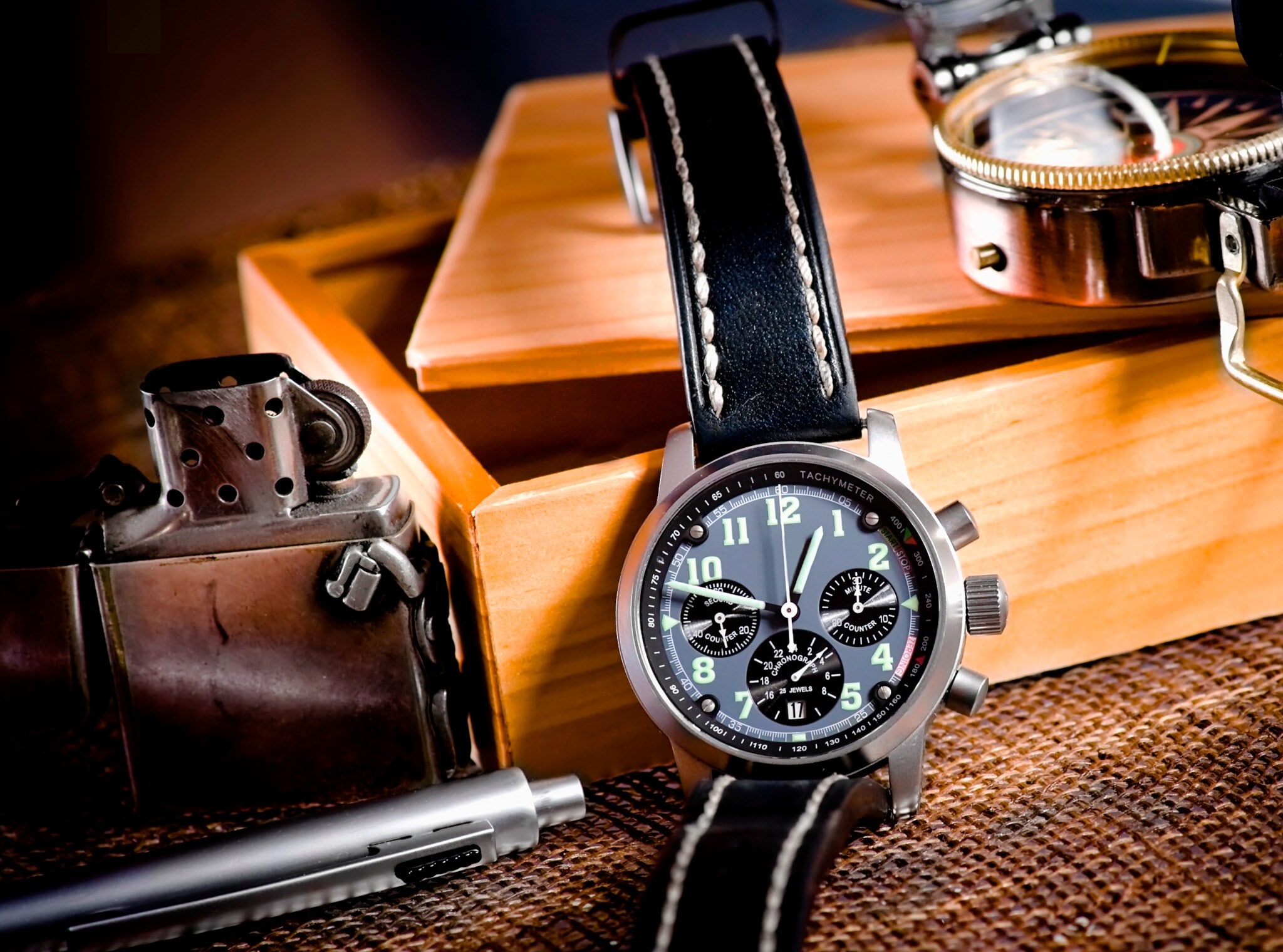 Ein Chronograf an einer Holzschachtel mit Kompass, Kuli und Feuerzeug Ein Chronograf an einer Holzschachtel mit Kompass, Kuli und Feuerzeug