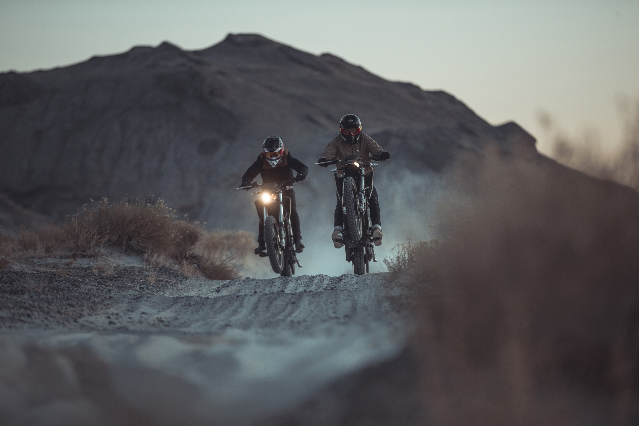 Zwei Motorradfahrer fahren in der Dämmerung durch eine Wüstenlandschaft Zwei Motorradfahrer fahren in der Dämmerung durch eine Wüstenlandschaft