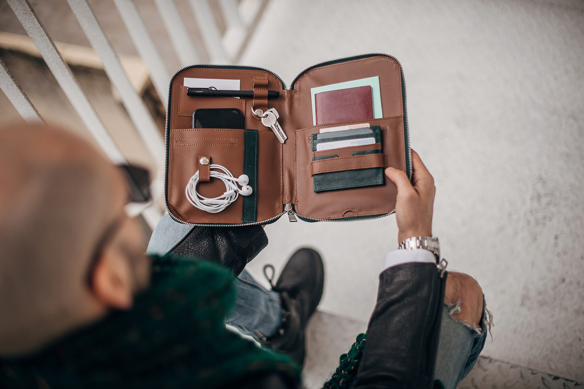 Eine sitzende Person von oben fotografiert, die eine Männerhandtasche aufklappt.