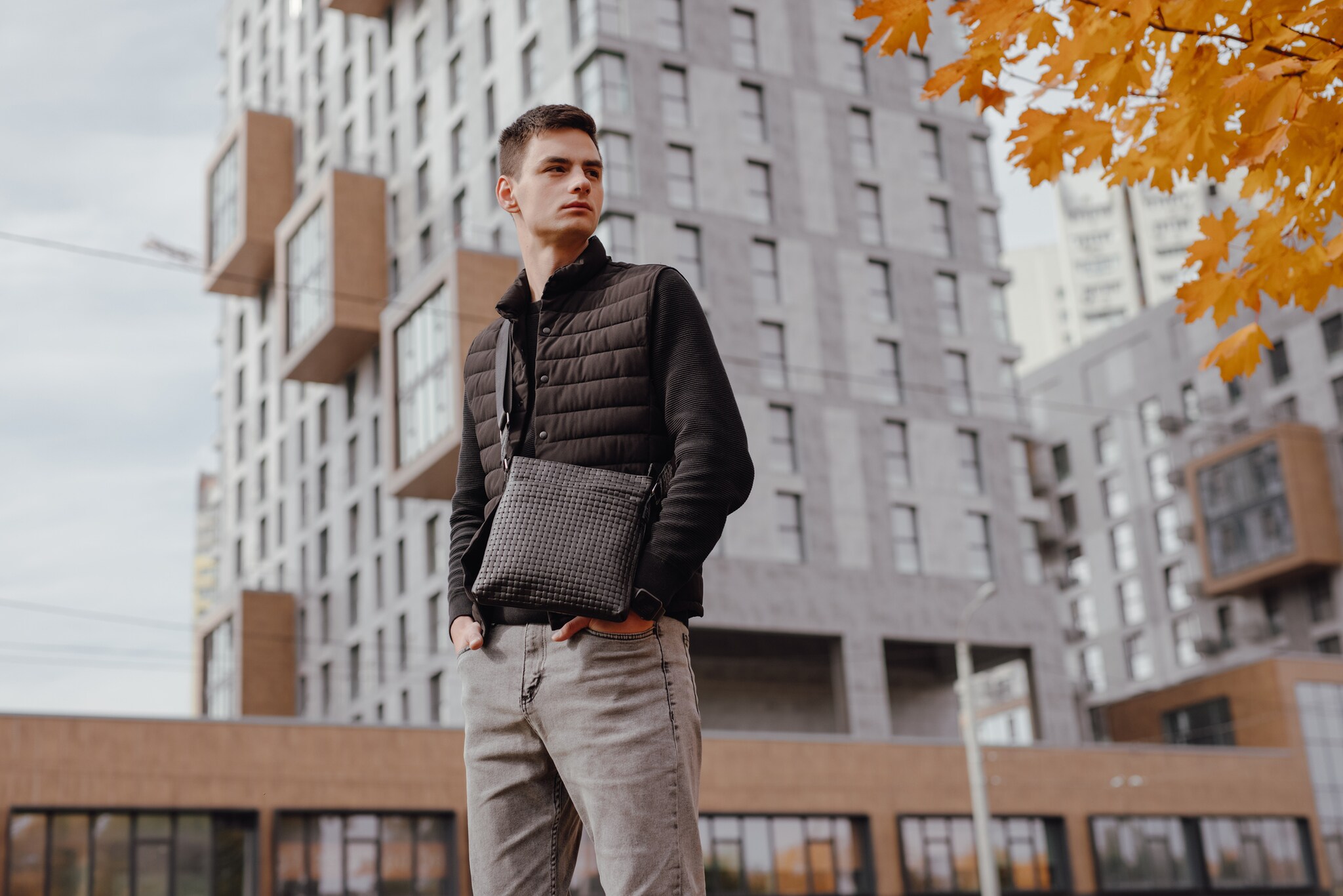 Fashion man holding black messenger bag in the autumn city