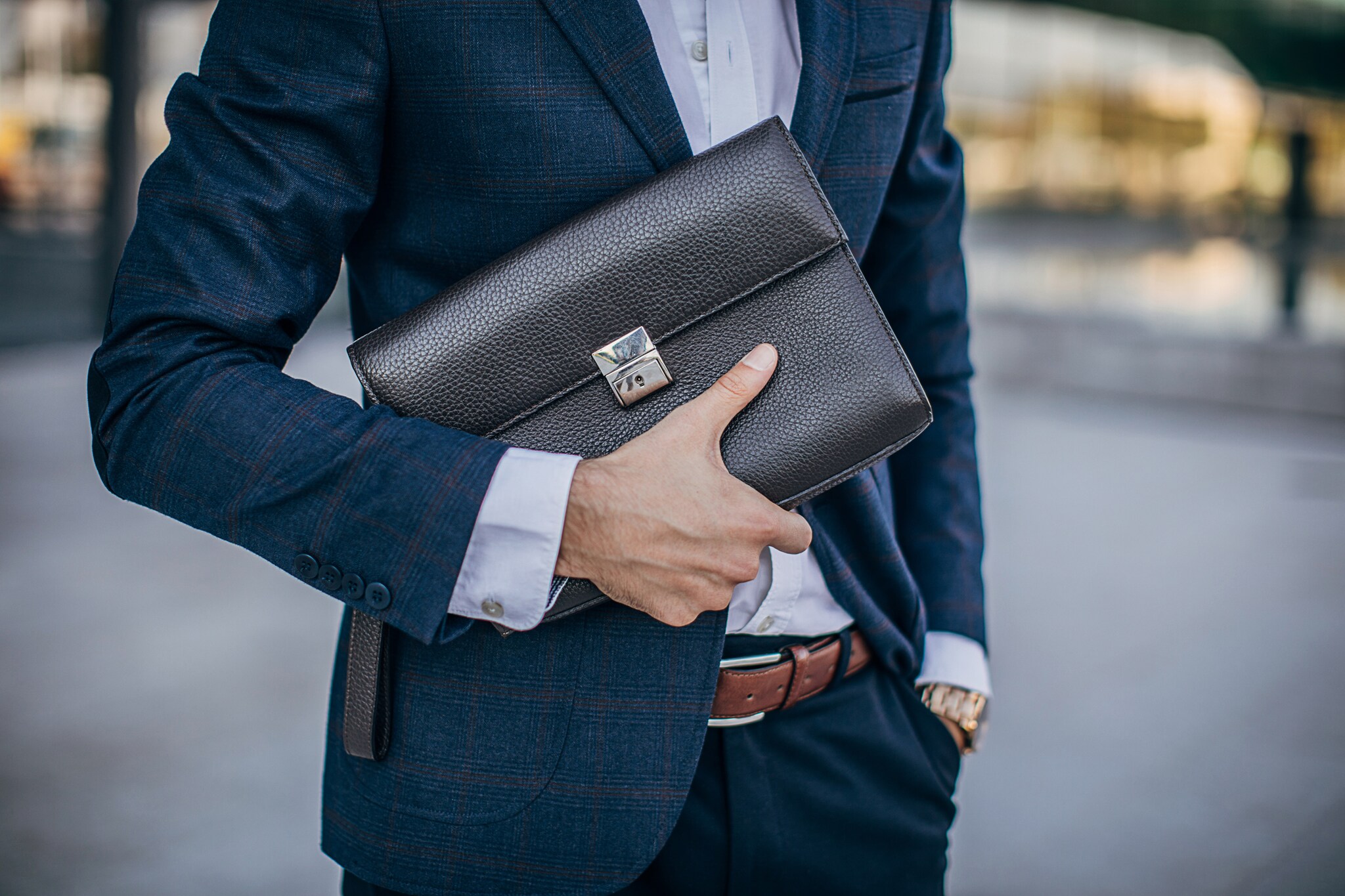 Detailaufnahme einer Person im Anzug, die eine Männerhandtasche aus Leder in der Hand hält.