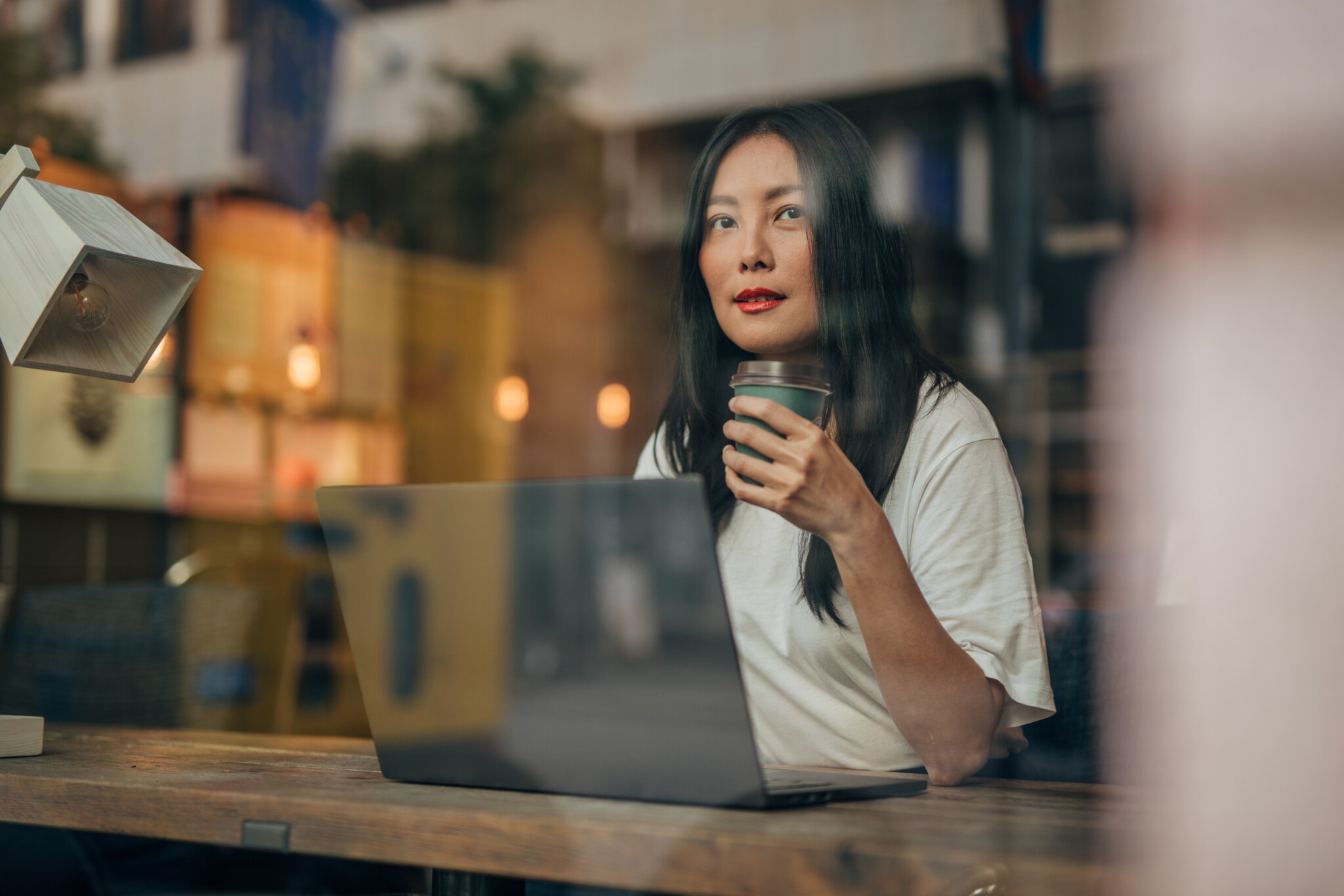 Eine Frau sitzt mit einem Coffee-to-go-Becher in einem Café am Laptop