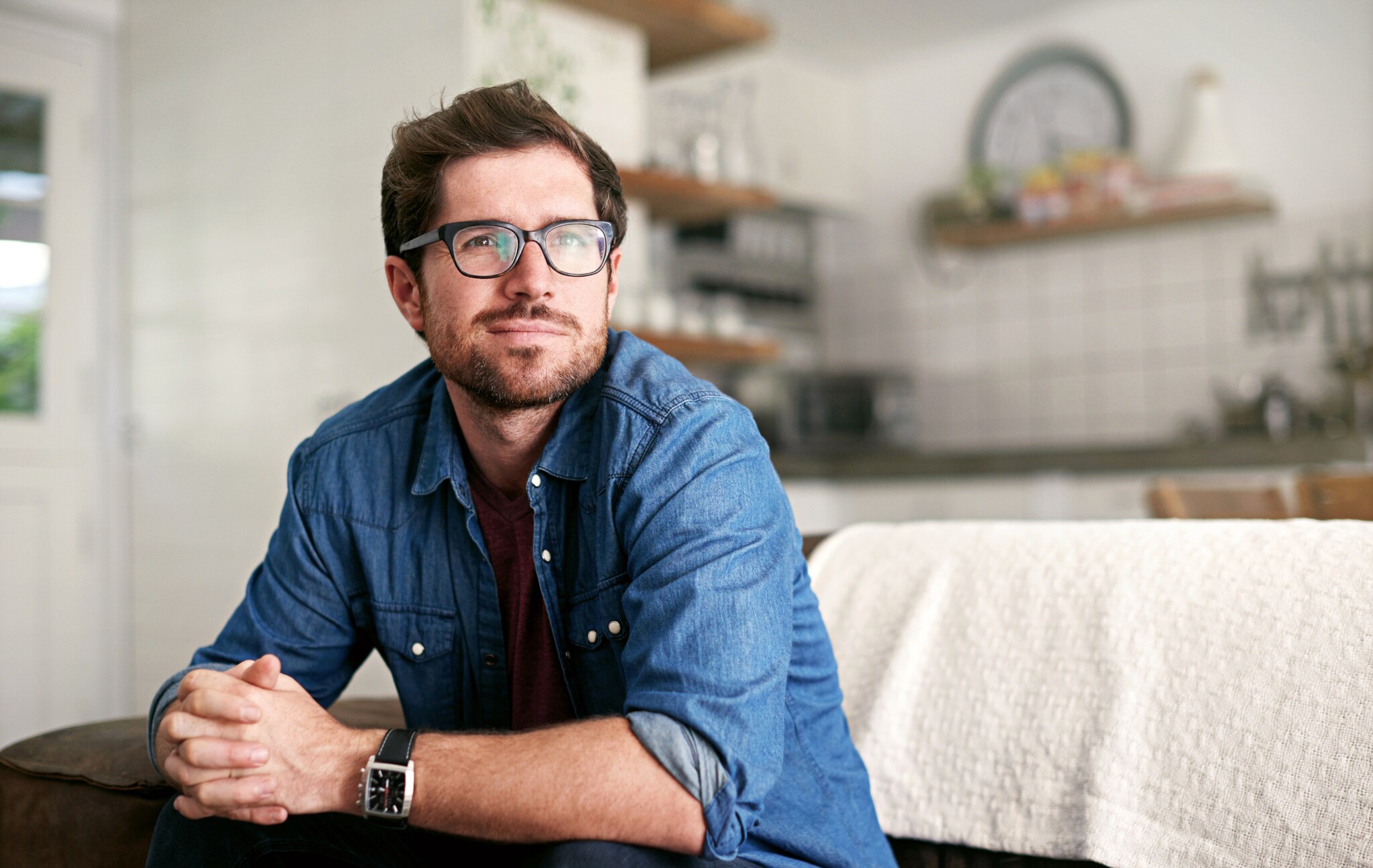 Eine Person sitzt mit ineinander verschränkten Händen lächelnd auf einem Sofa