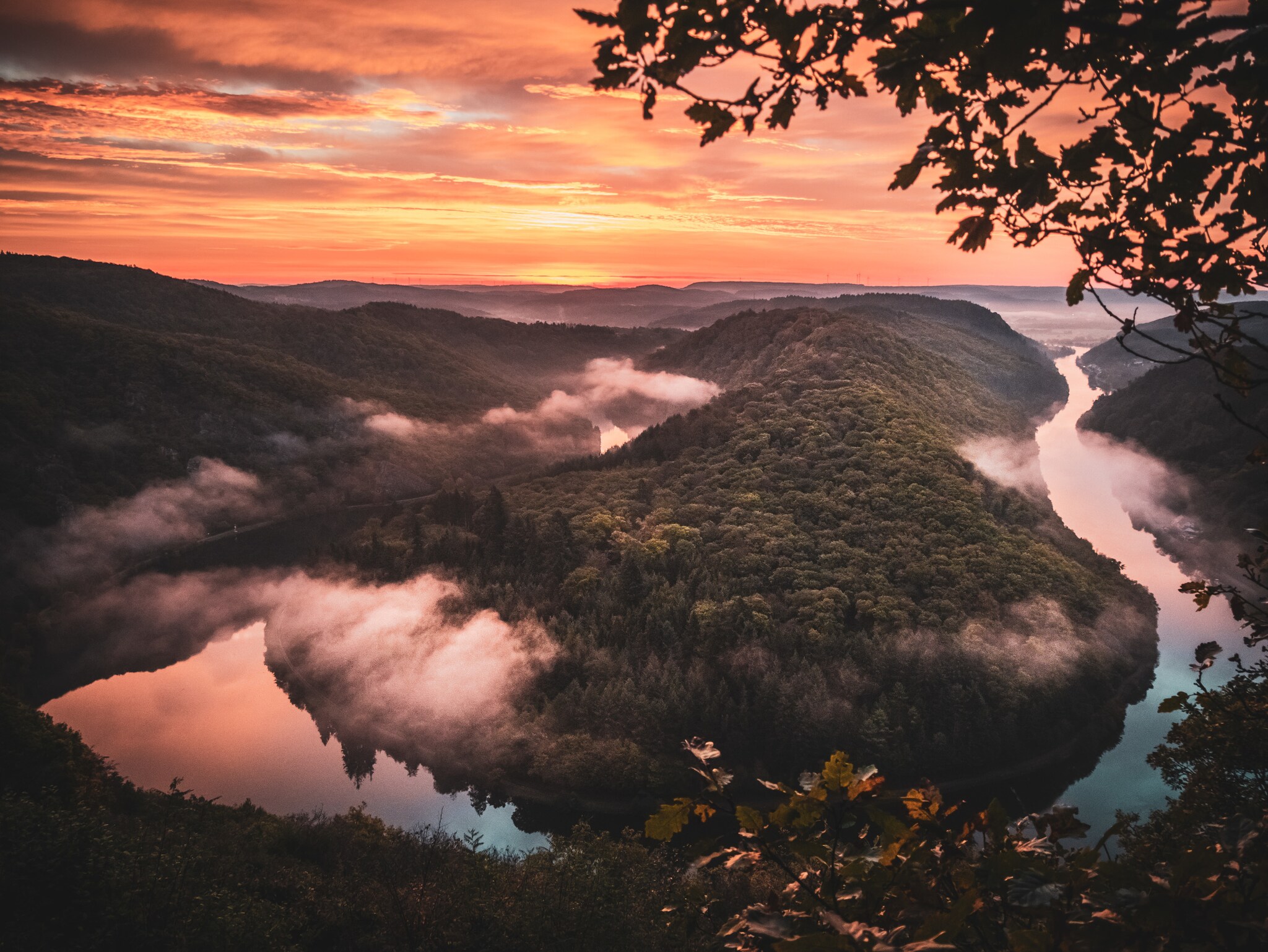 Sonnenaufgang über einem hügeligen Gebiet, durch das sich ein Fluss zieht