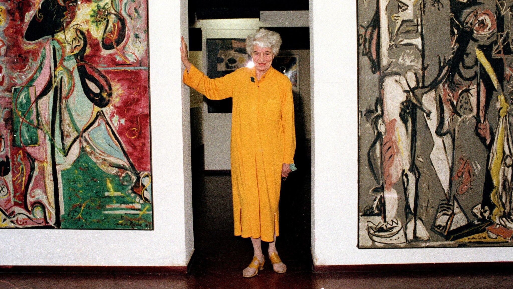 Porträt von Peggy Guggenheim in einem gelben Kleid zwischen zwei abstrakten Gemälden