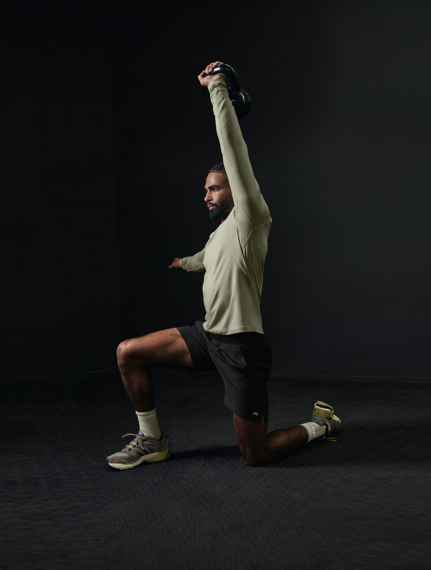 Eine Person kniet mit einem Bein, streckt einen Arm seitlich aus und hält mit dem anderen eine Kettlebell hoch Eine Person kniet mit einem Bein, streckt einen Arm seitlich aus und hält mit dem anderen eine Kettlebell hoch