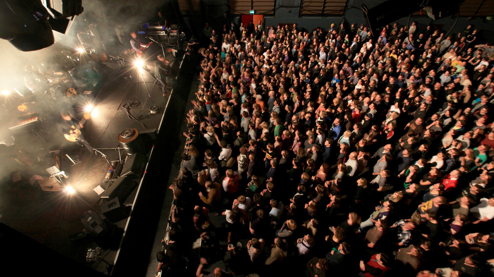Eine Band spielt auf einer Bühne vor Publikum in einer Konzerthalle, Aufnahme aus der Vogelperspektive Eine Band spielt auf einer Bühne vor Publikum in einer Konzerthalle, Aufnahme aus der Vogelperspektive