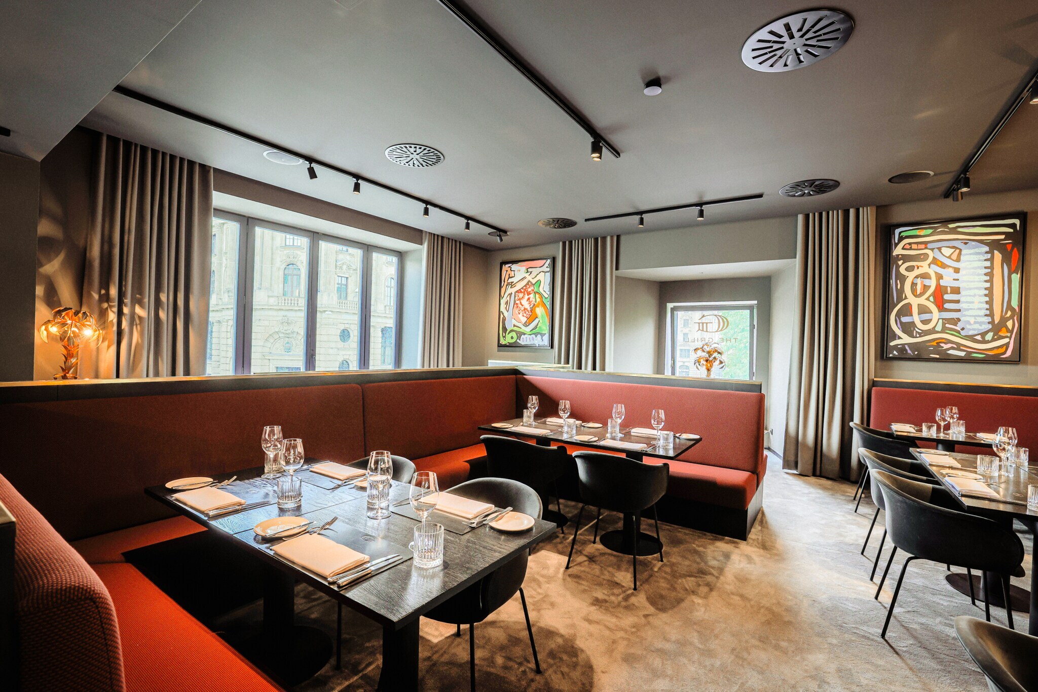 Blick in das Innere eines Restaurants mit eingedeckten Tischen und roten Sitzbänken.