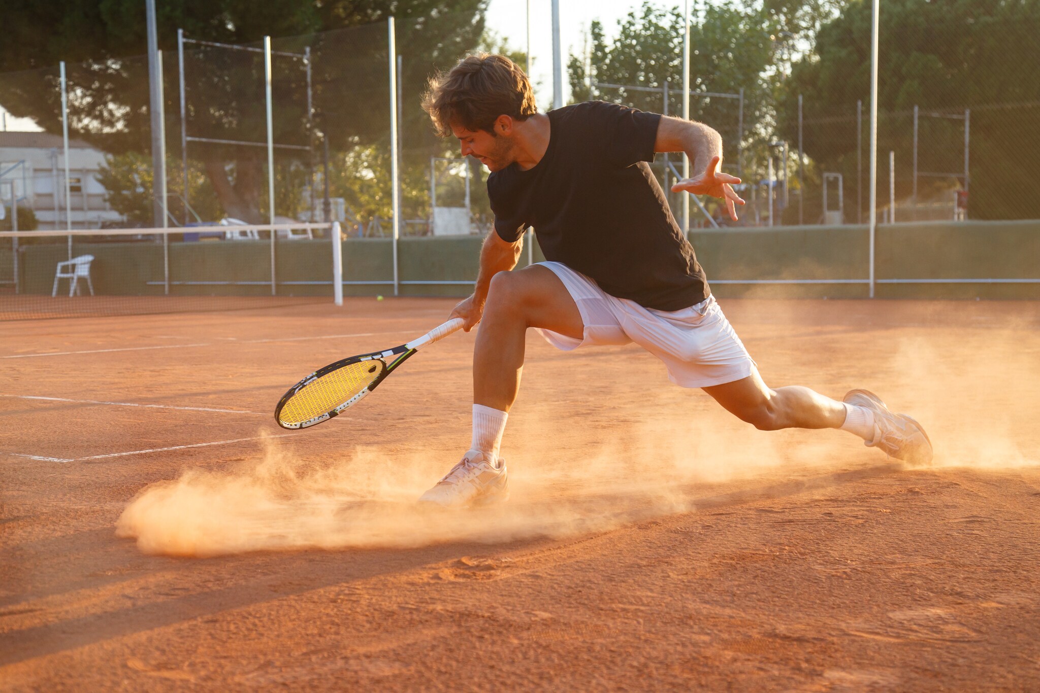 Eine Person mit Tennisschläger in der Hand bremst auf einem roten Schotterplatz.