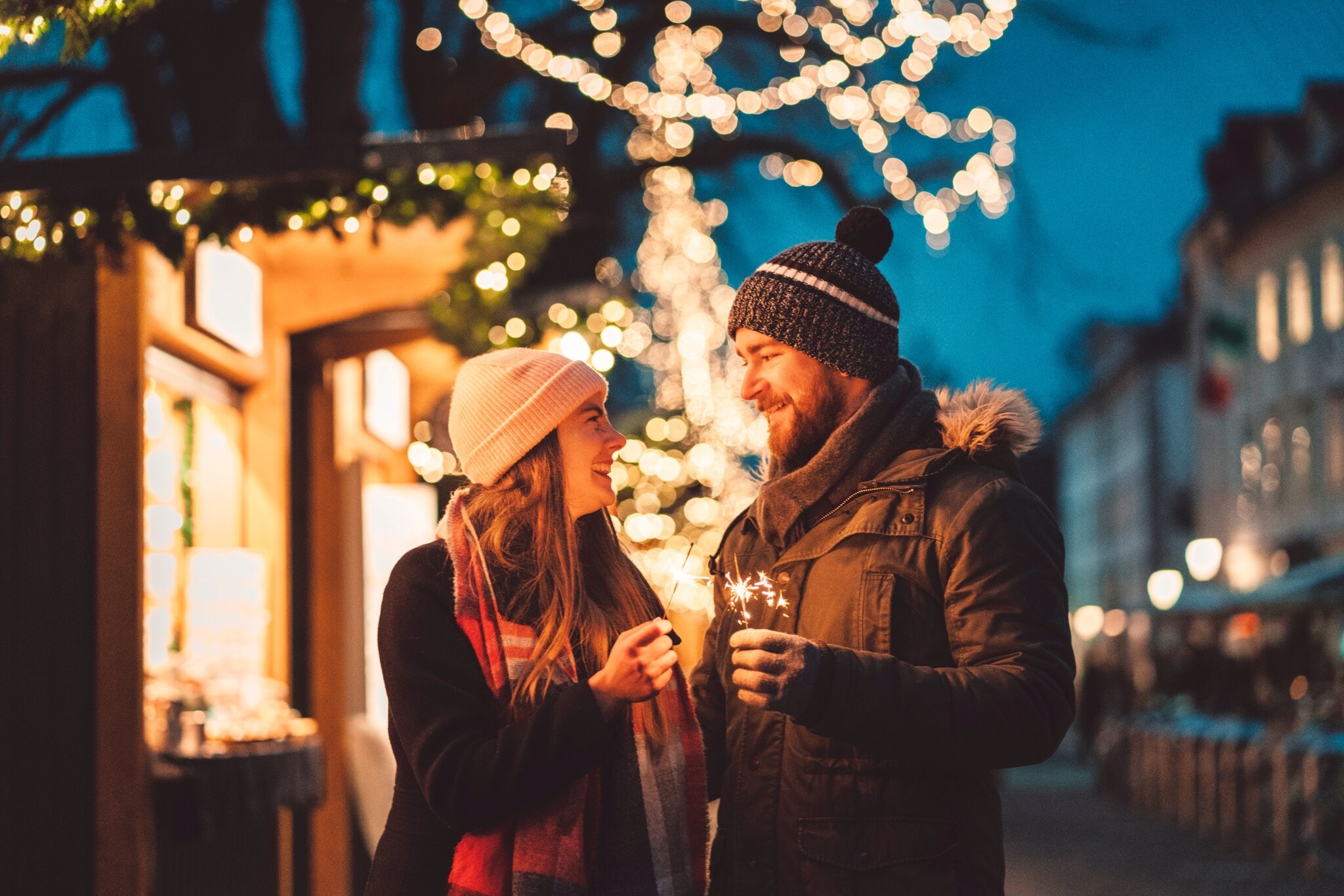 Eine Frau und ein Mann stehen auf dem Weihnachtsmarkt und schauen sich an, in ihren Händen halten sie Wunderkerzen Eine Frau und ein Mann stehen auf dem Weihnachtsmarkt und schauen sich an, in ihren Händen halten sie Wunderkerzen