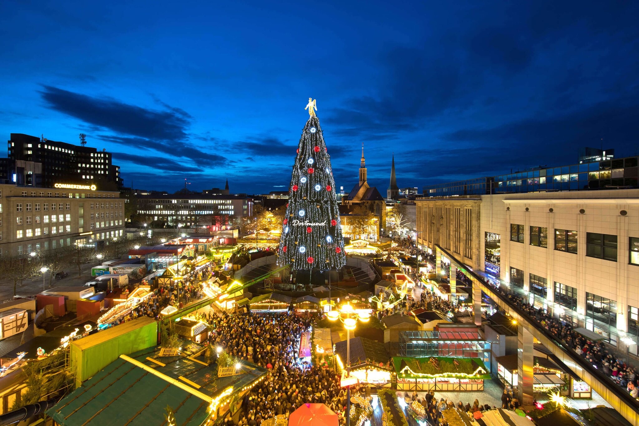 Blick von oben auf einen Weihnachtsmarkt in dessen Mitte ein riesiger beleuchteter Weihnachtsbaum steht Blick von oben auf einen Weihnachtsmarkt in dessen Mitte ein riesiger beleuchteter Weihnachtsbaum steht