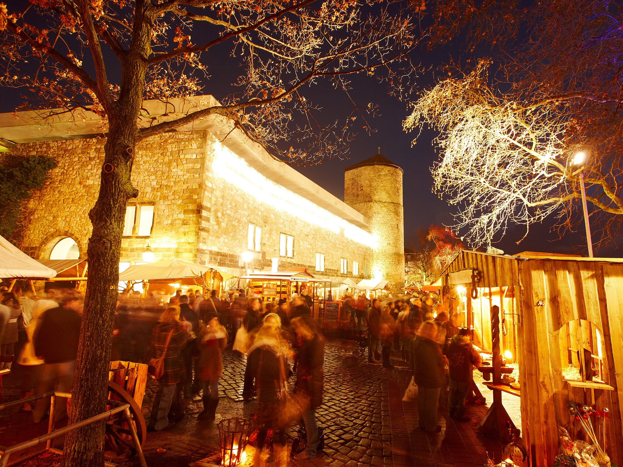 Beleuchtete historische Mauern, vor denen sich Menschen tummeln und Stände besuchen Beleuchtete historische Mauern, vor denen sich Menschen tummeln und Stände besuchen