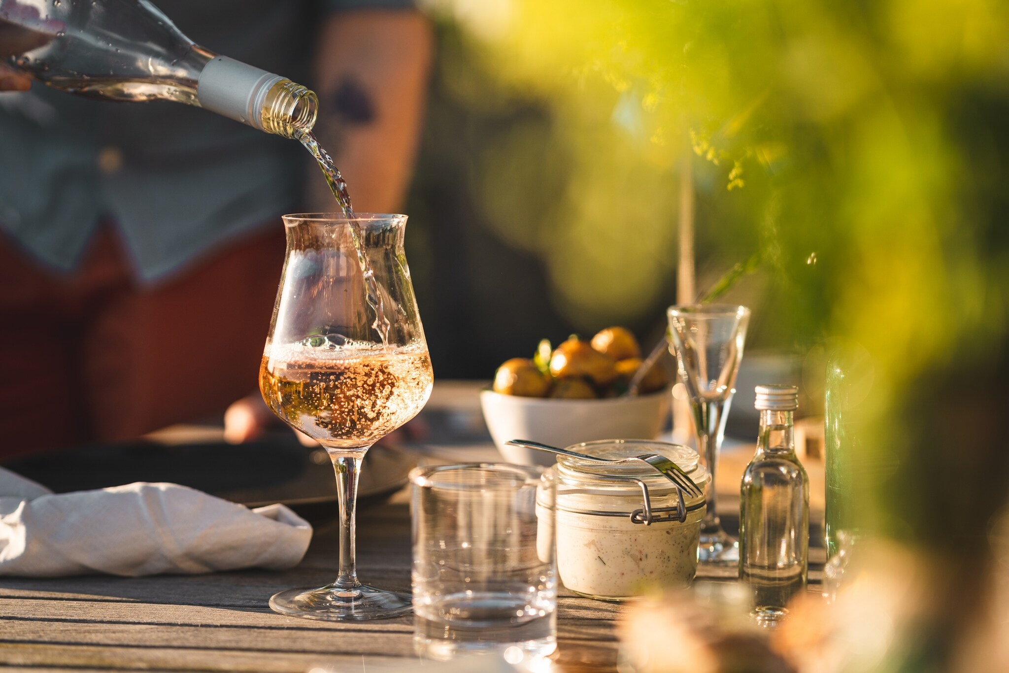 Ein Glas auf einem gedeckten Gartentisch, in das Rosé eingeschenkt wird Ein Glas auf einem gedeckten Gartentisch, in das Rosé eingeschenkt wird