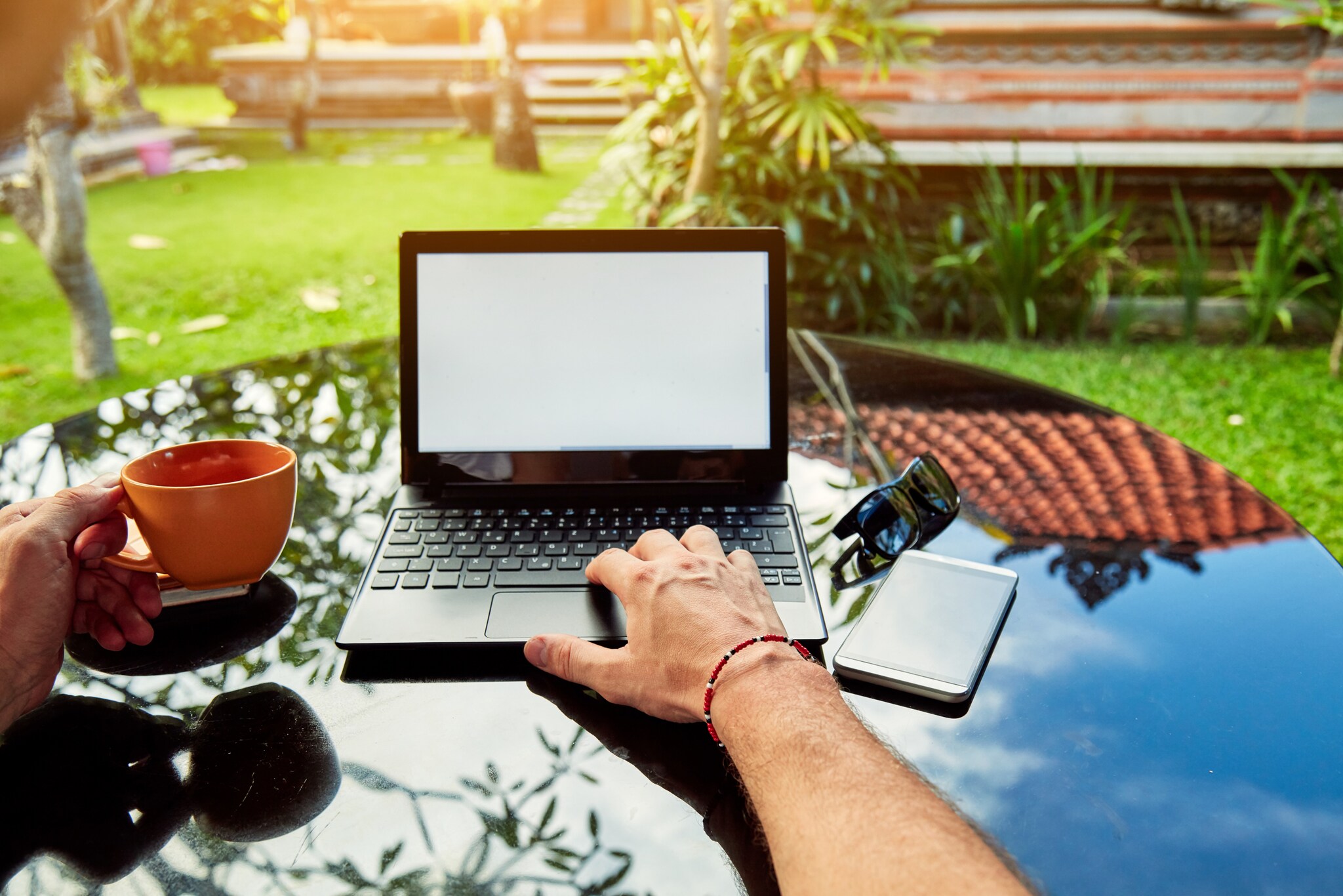 Blick auf einen Laptop, der auf einem Tisch in einem tropischen Garten steht.