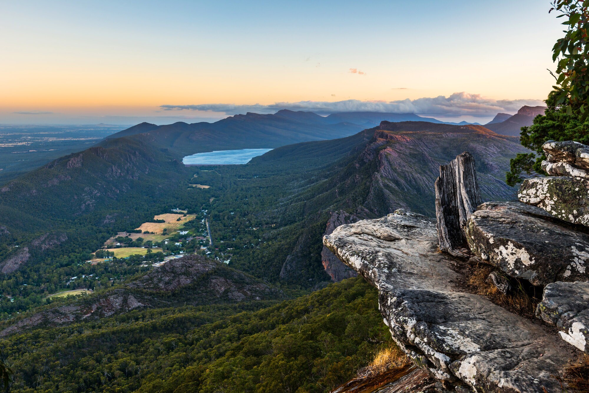 Blick in eine zerklüftete, grüne Berglandschaft mit See von einem Felsvorsprung