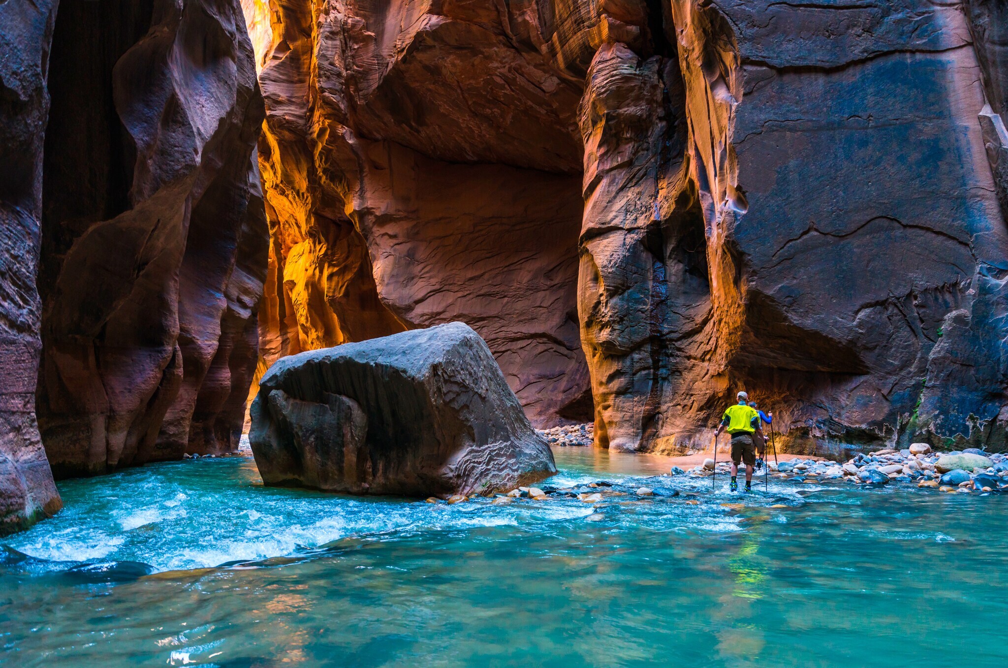 Zwei Wanderer waten durch einen Fluß zwischen Felswänden