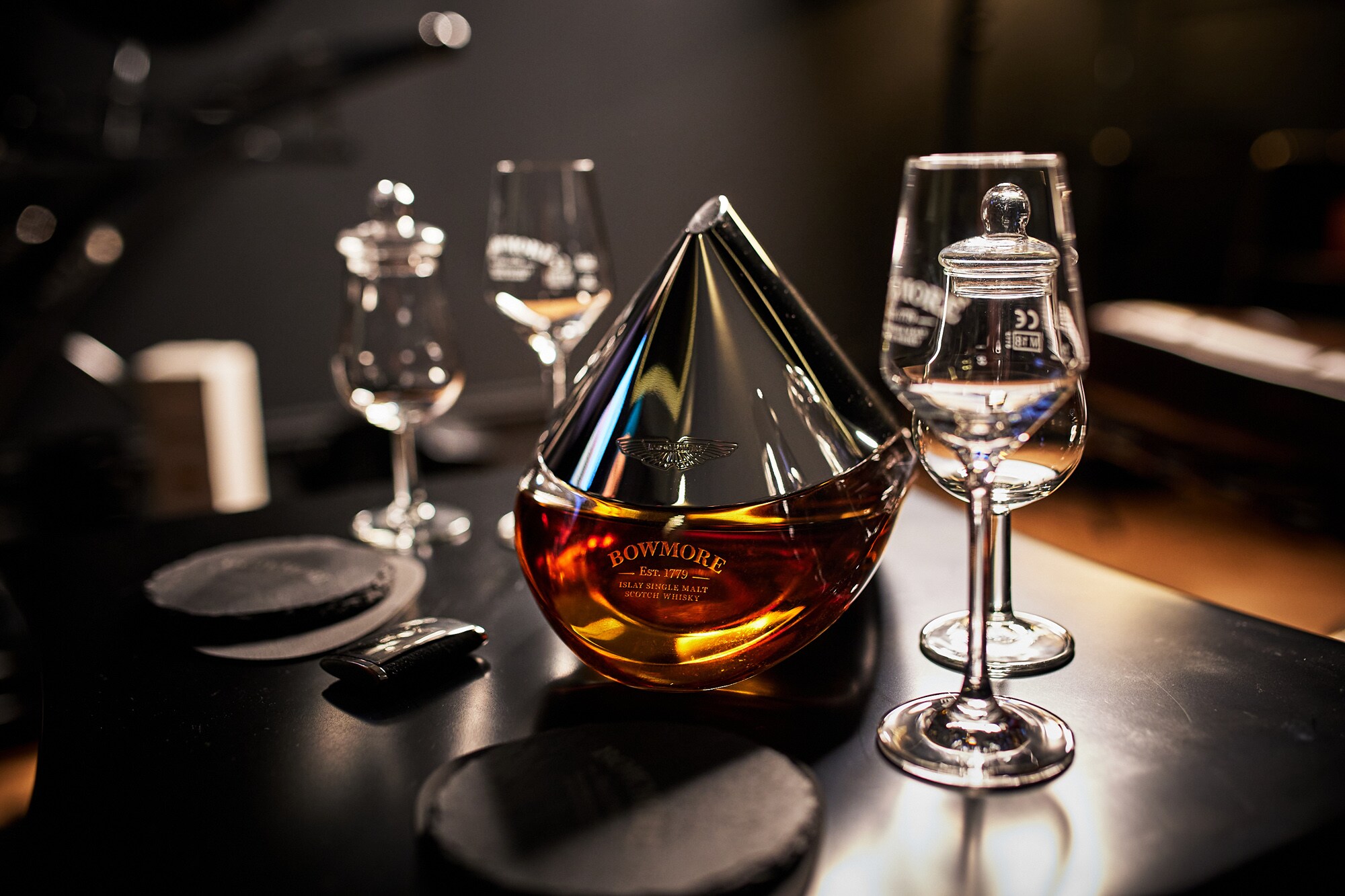 Eine Flasche Bowmore ARC-52 aus der Kooperation mit Aston Martin steht auf einem Tisch mit speziellen Whisky-Gläsern