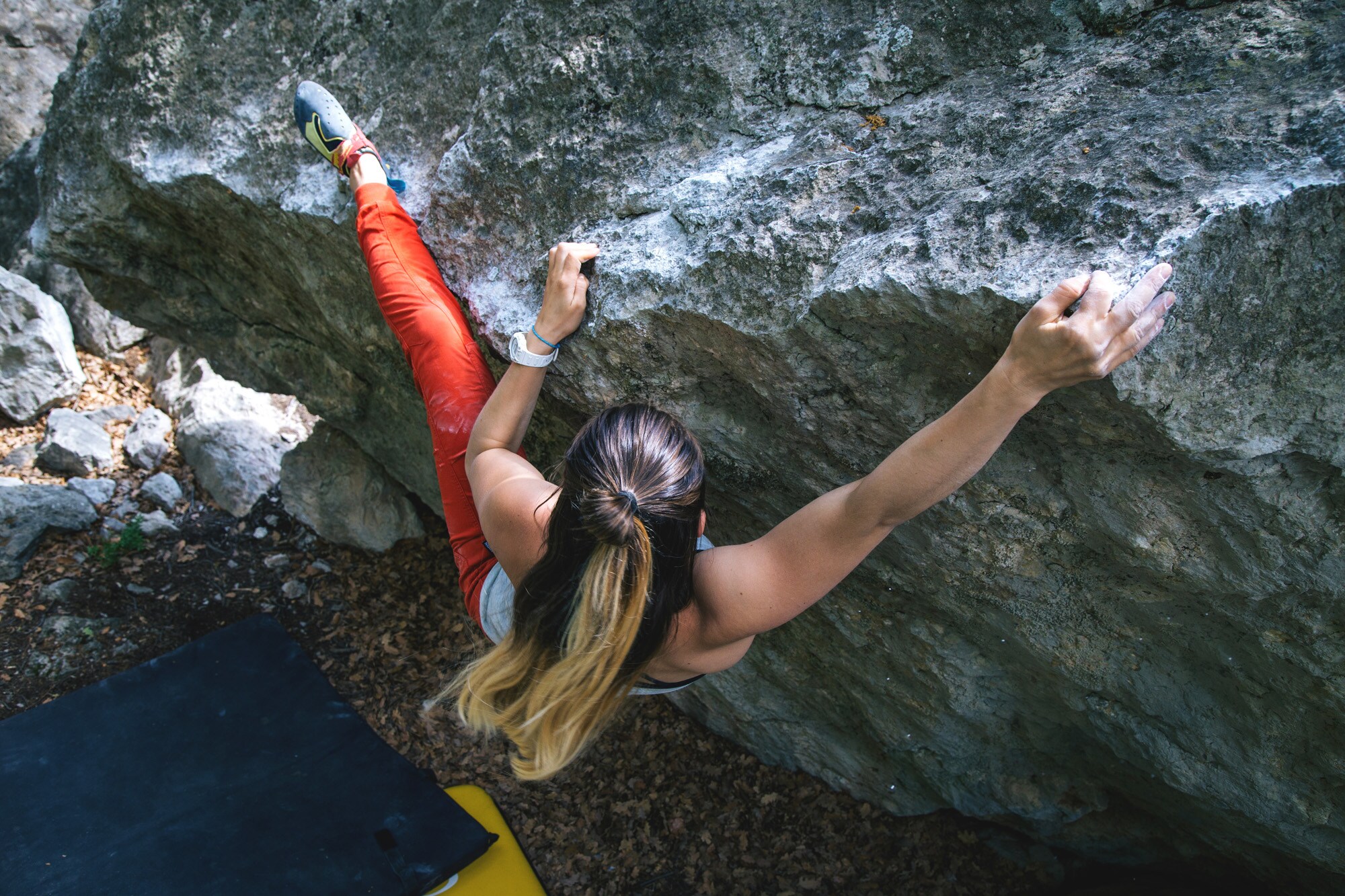 Blick von oben auf eine Person mit langen Haaren, die an einer Felswand bouldert