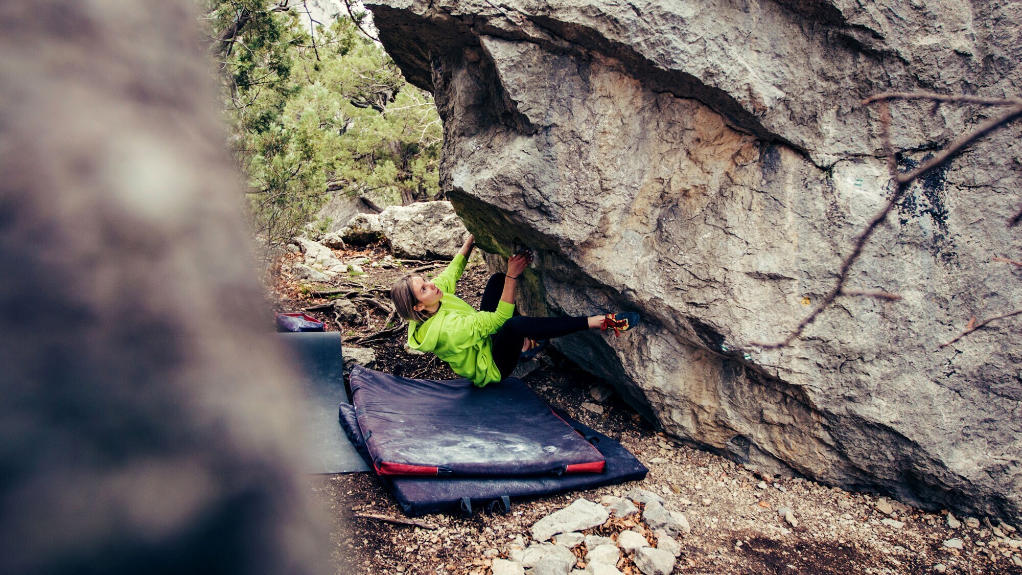 Eine Person bouldert an einer Felswand, unter ihr liegt eine weiche Matte.