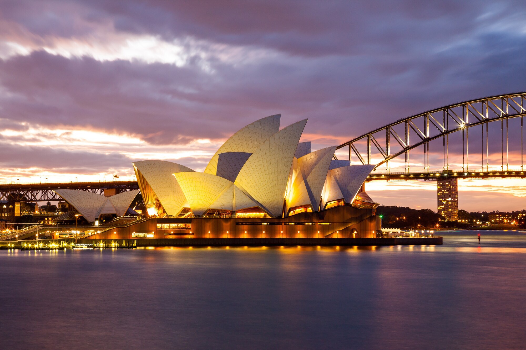 Beleuchtetes Sydney Opera House mit Harbour Bridge in der Abenddämmerung Beleuchtetes Sydney Opera House mit Harbour Bridge in der Abenddämmerung