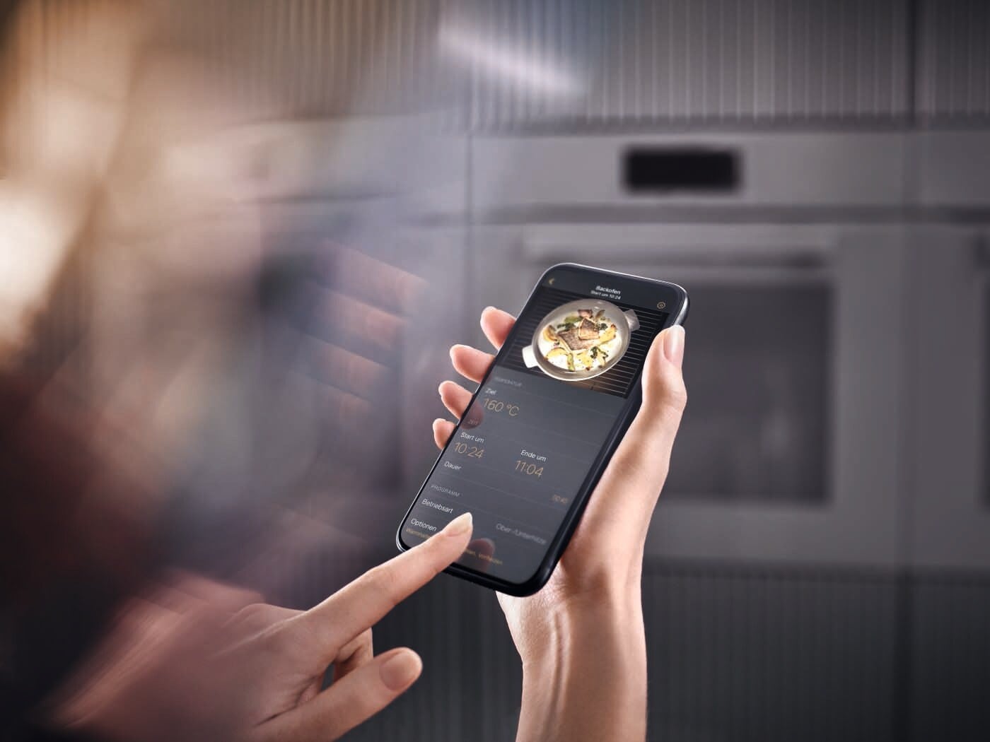 Eine Frau bedient einen smarten Backofen per Smartphone Eine Frau bedient einen smarten Backofen per Smartphone