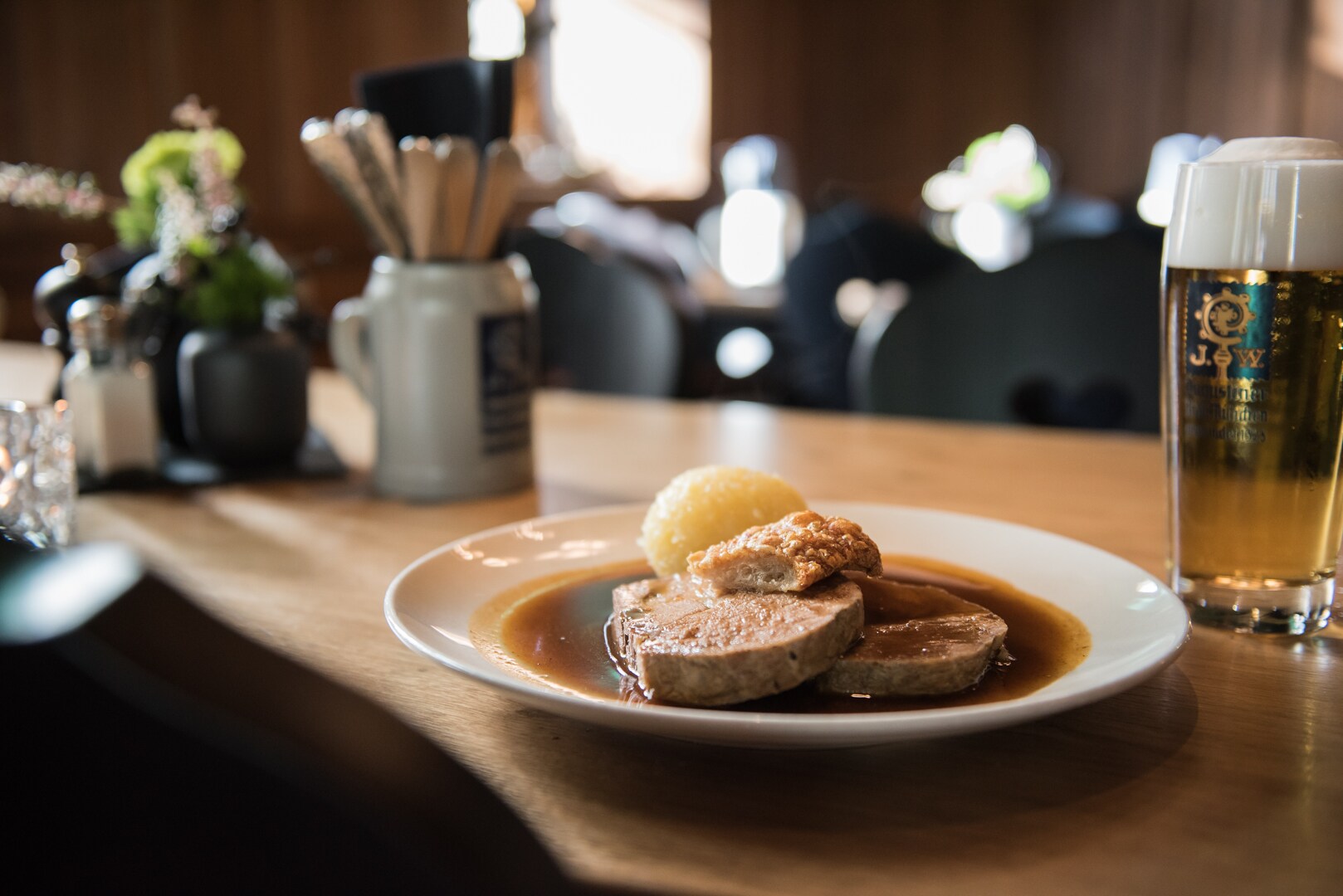 Ein Stück Fleisch mit Knödel auf einem Teller, daneben ein Bier.