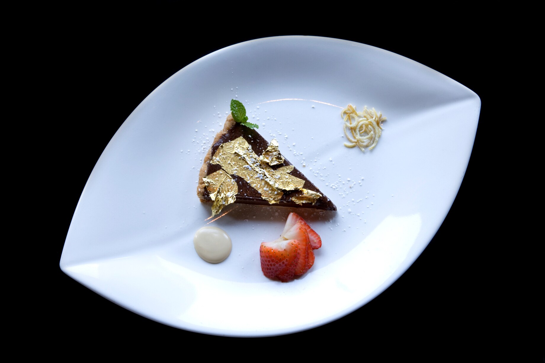 Ein weißer Teller mit einem Stück Schokokuchen, garniert mit Blattgold