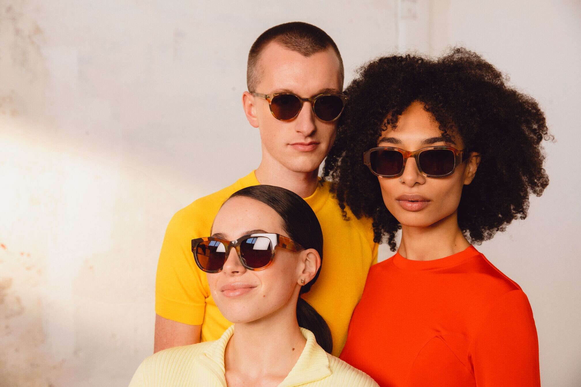 Drei Personen mit einfarbigen Oberteilen und Sonnenbrillen
