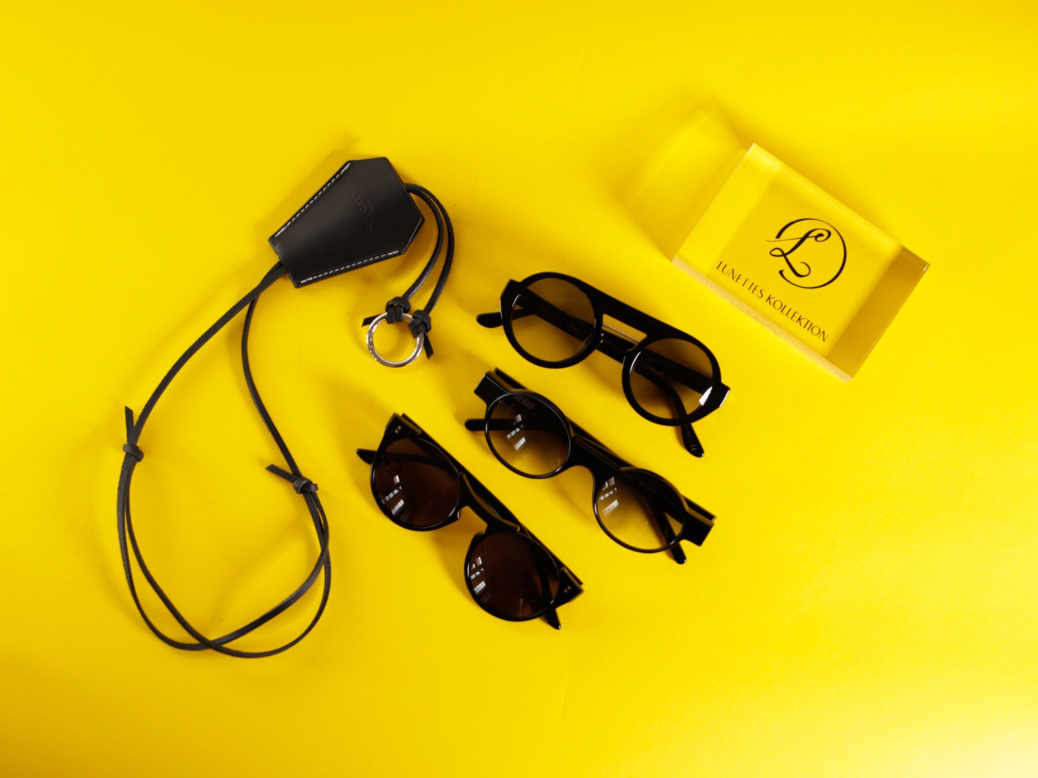 Mehrere Brillen und Zubehör liegen auf gelbem Untergrund