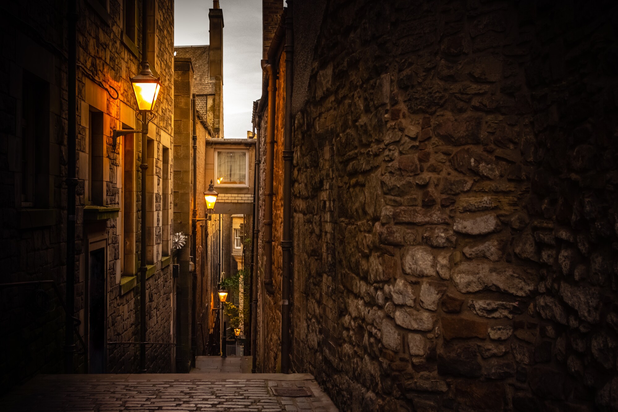 Dunkle Gasse in Edinburgh, die von Straßenlaternen schwach beleuchtet wird.
