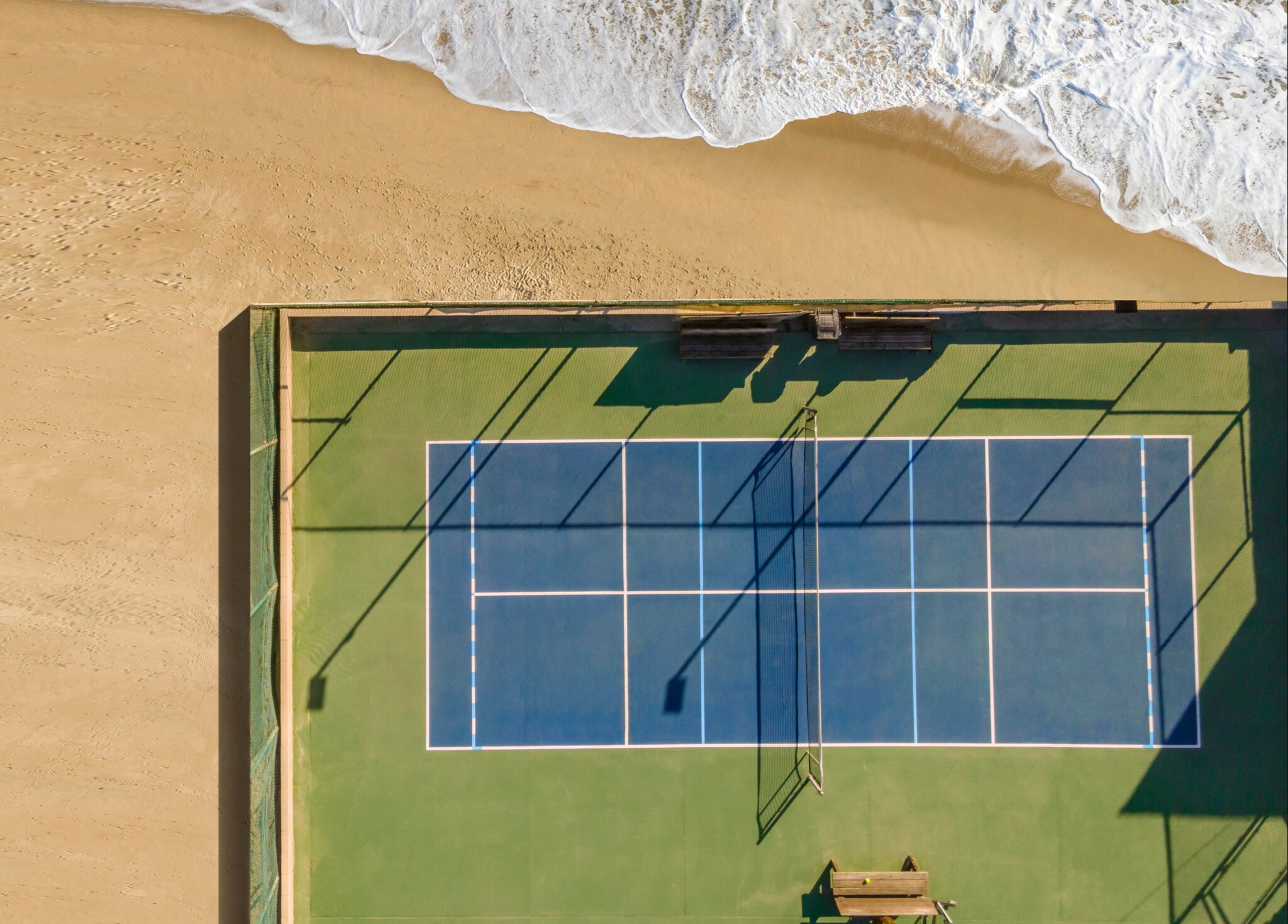 Drohnenansicht des Tennisplatzes am Sand und Meer.