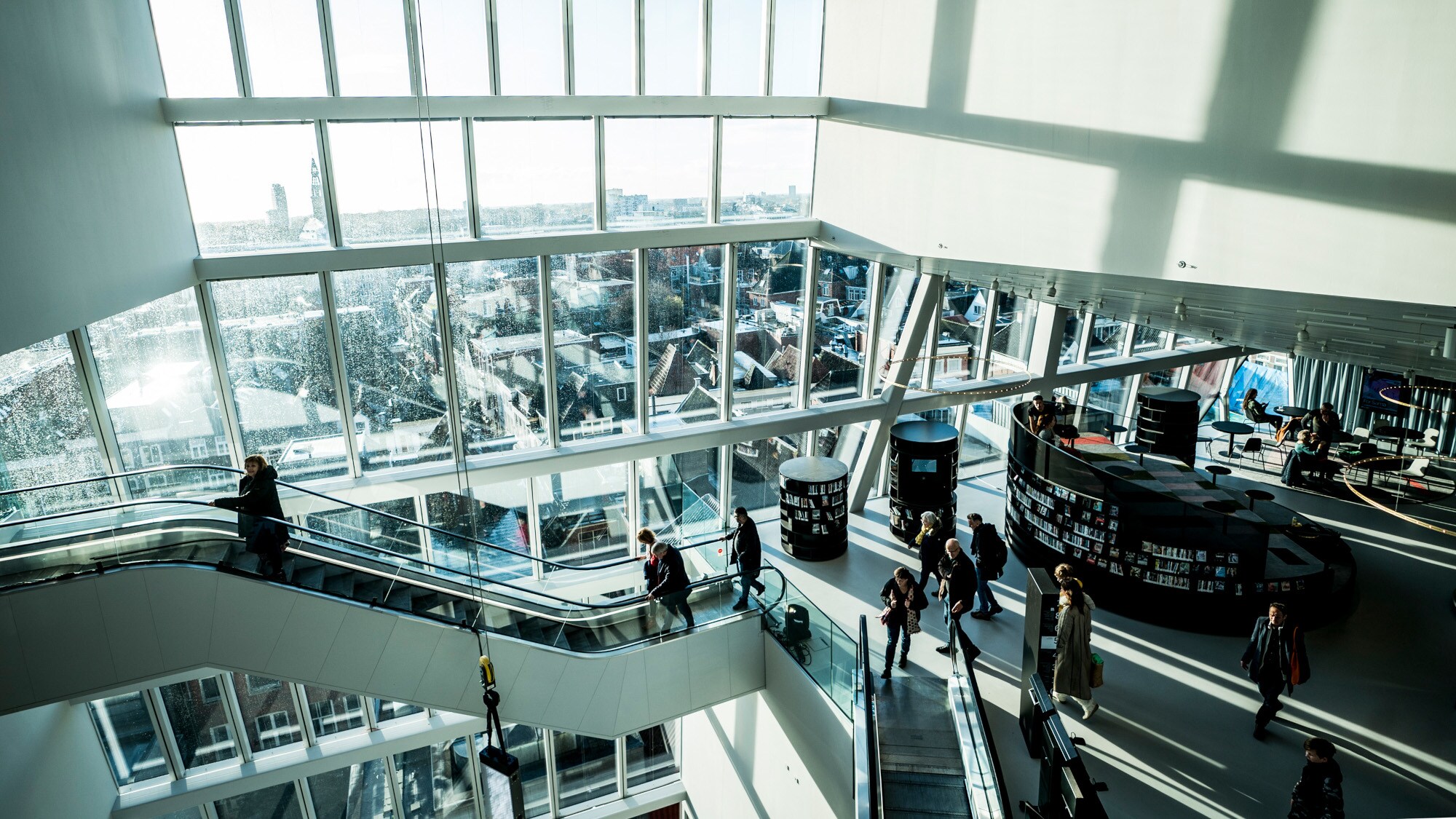 Innenaufnahme eines modernen Gebäudekomplexes mit Personen auf Rolltreppen und Panoramablick über eine Stadt