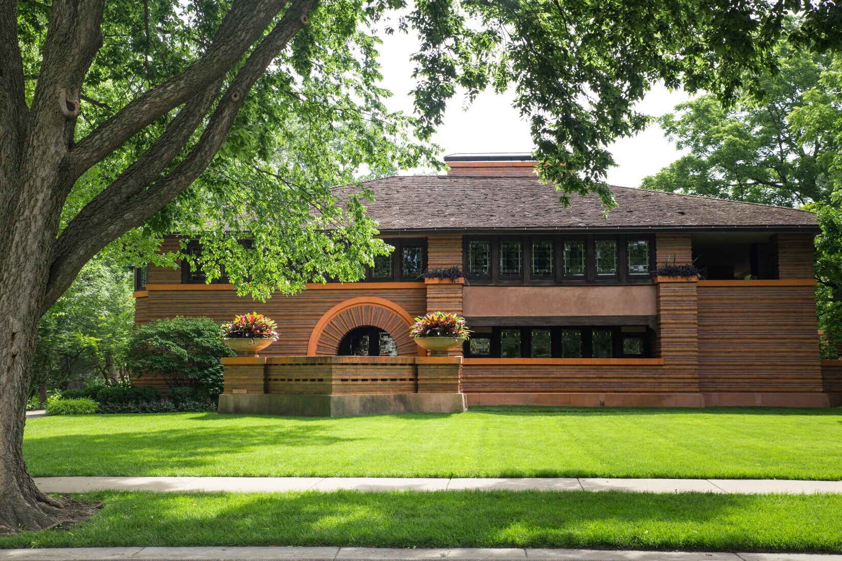 Ein braunes Steinhaus, entworfen von Frank Lloyd Wright, umrahmt von großen Bäumen